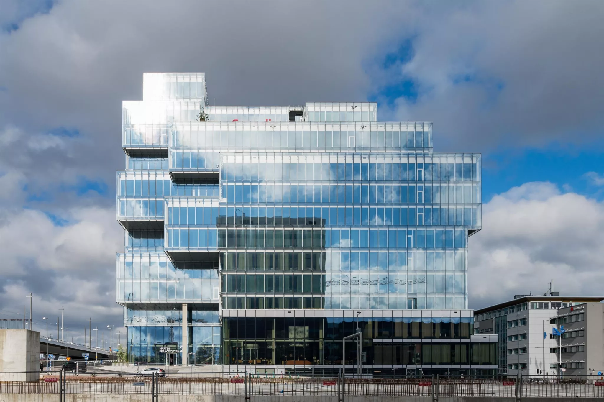 Glasbyggnad med reflektioner av himlen, med geometriska utskjutande delar och moln i bakgrunden.