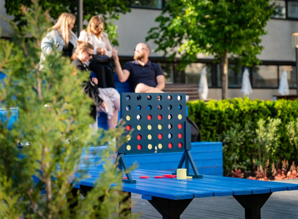 4. Fyra personer spelar ett stort brädspel utomhus på ett blått bord i en grönskande park.