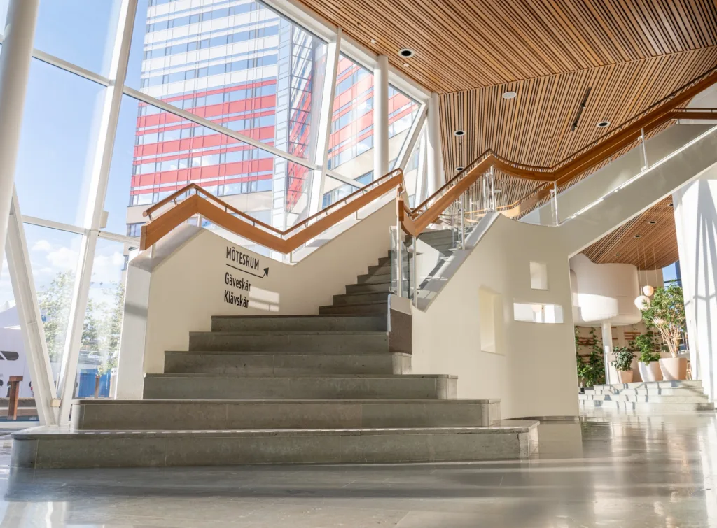 2. Modern trappa i en ljus byggnad med stora glasväggar och träpanel i taket.