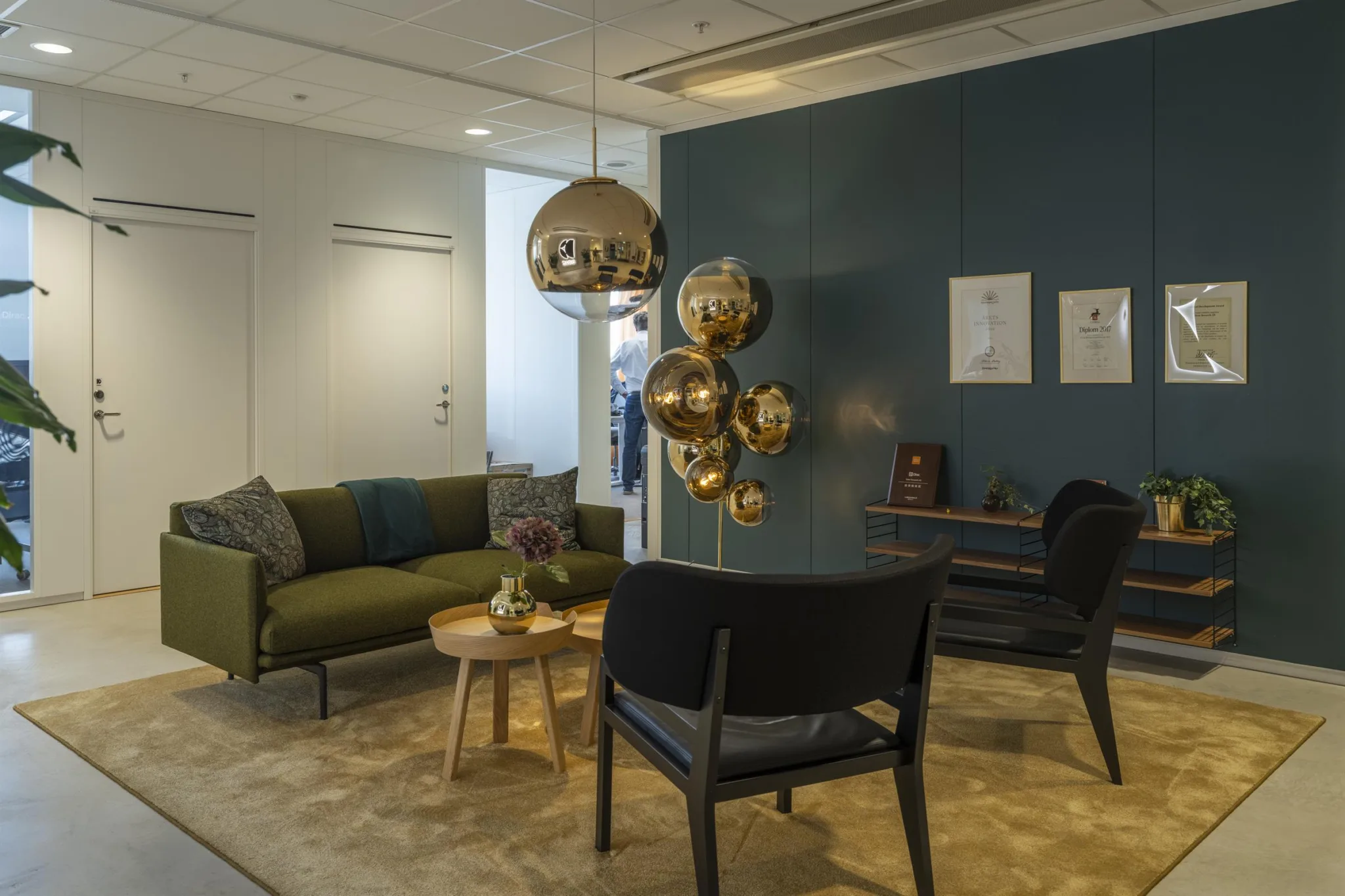 3. Ett stilfullt loungeområde med gröna soffor, svarta stolar, ett bord med dekor och en blå vägg med konstverk.