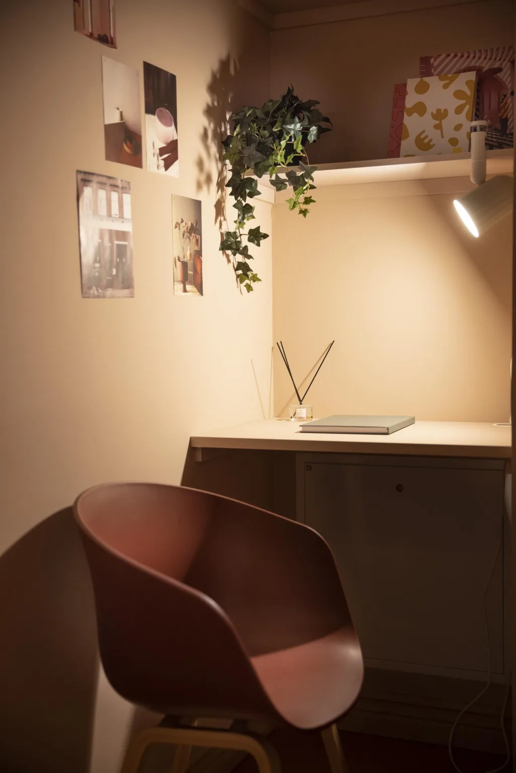 1. Ett litet skrivbord med en laptop, väggdekorationer och en hängande växt, bredvid en brun stol under varm belysning.