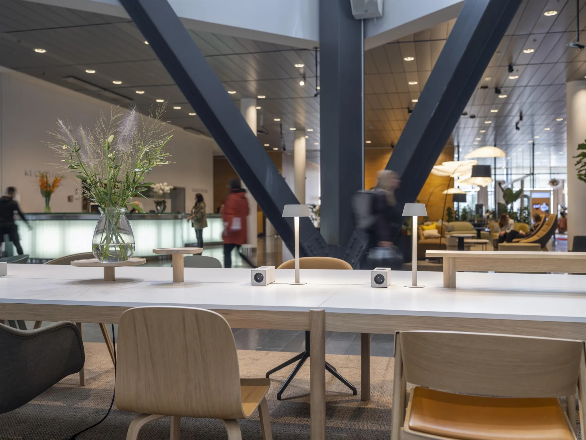 Ett modernt café med sittplatser, bordslampor och växter, samt människor i bakgrunden.