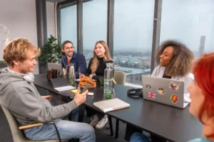 Fyra personer sitter runt ett konferensbord och verkar diskutera, med utsikt över en stad genom stora fönster.