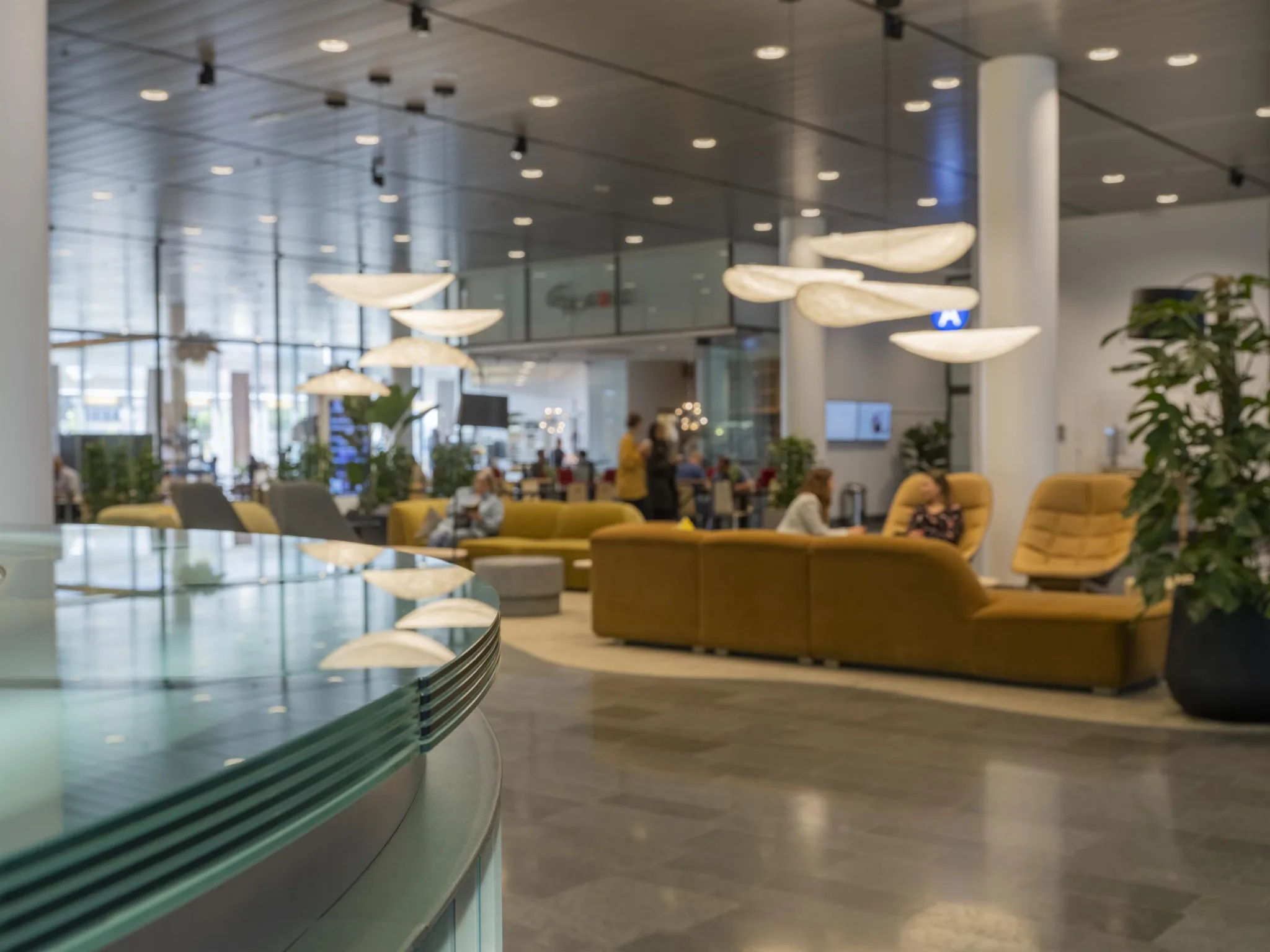 En modern lobby med bekväma soffor, dekorativa taklampor och människor som samtalar.