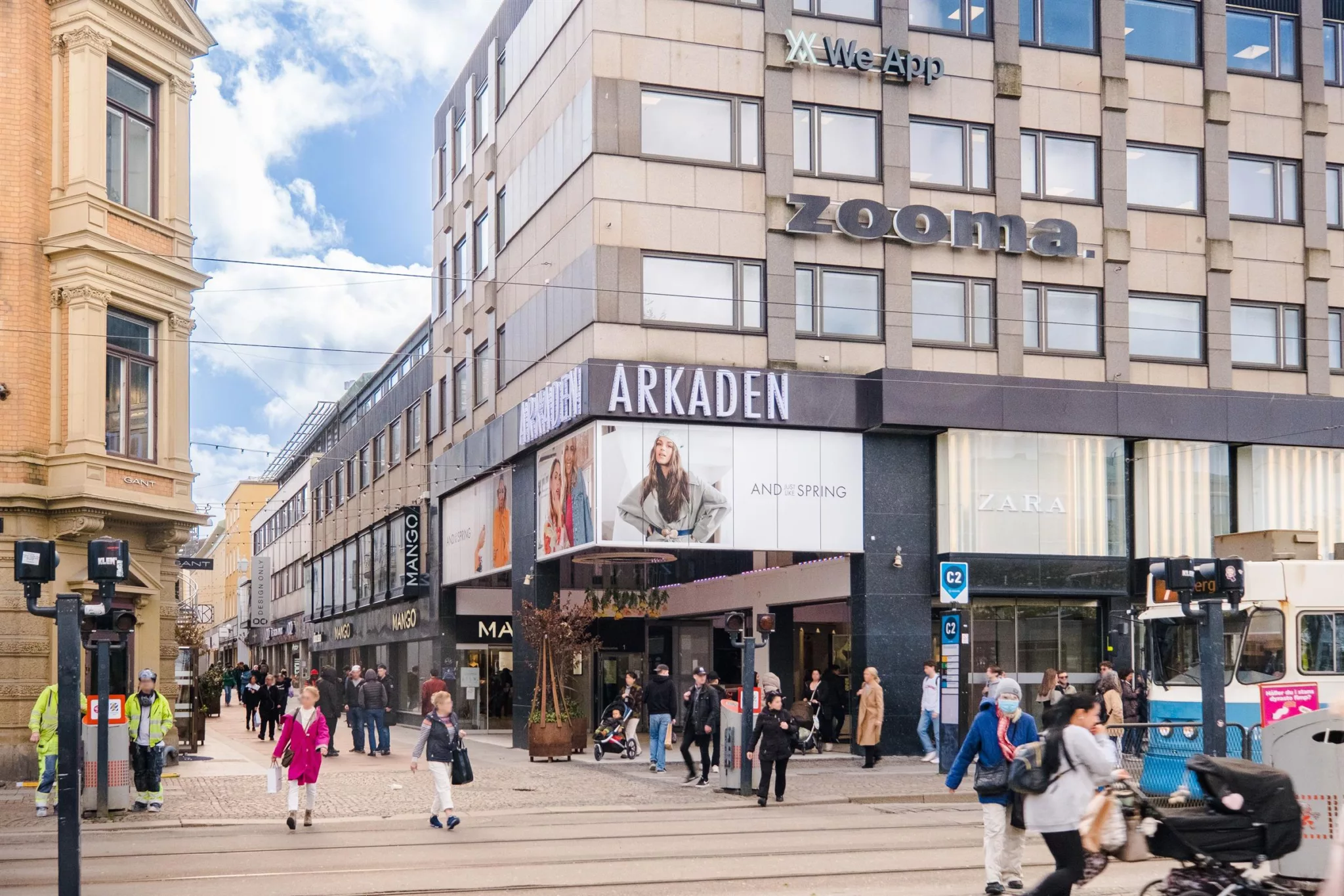 En livlig shoppinggata med människor, butiker och en stor skylt med texten "ARKADEN".