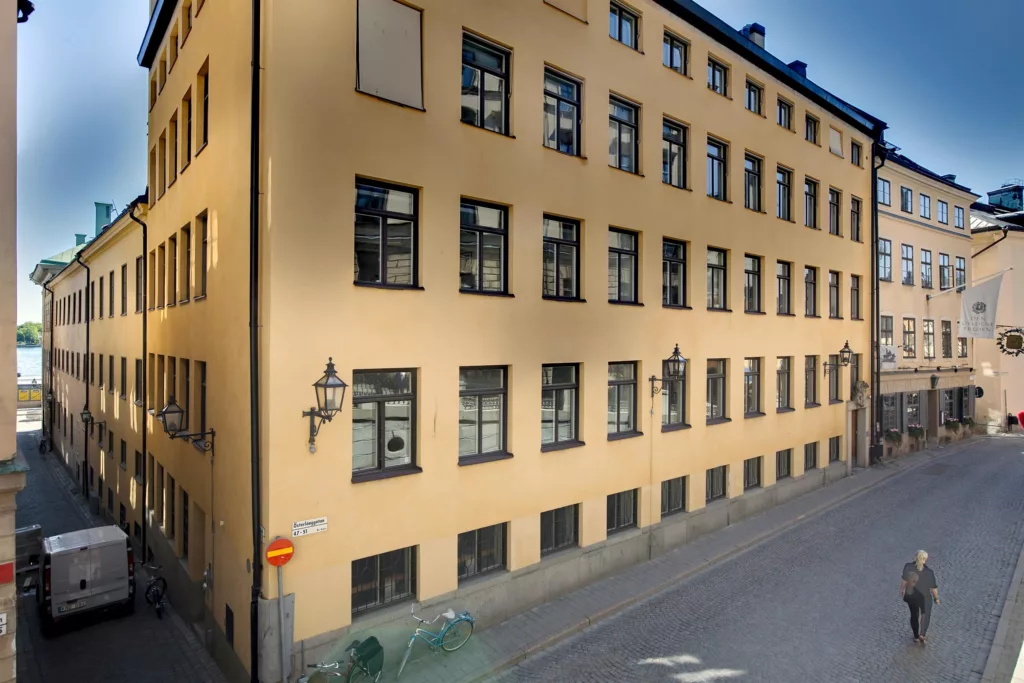 En gul byggnad med många fönster, vid en trottoar med gatubelysning.