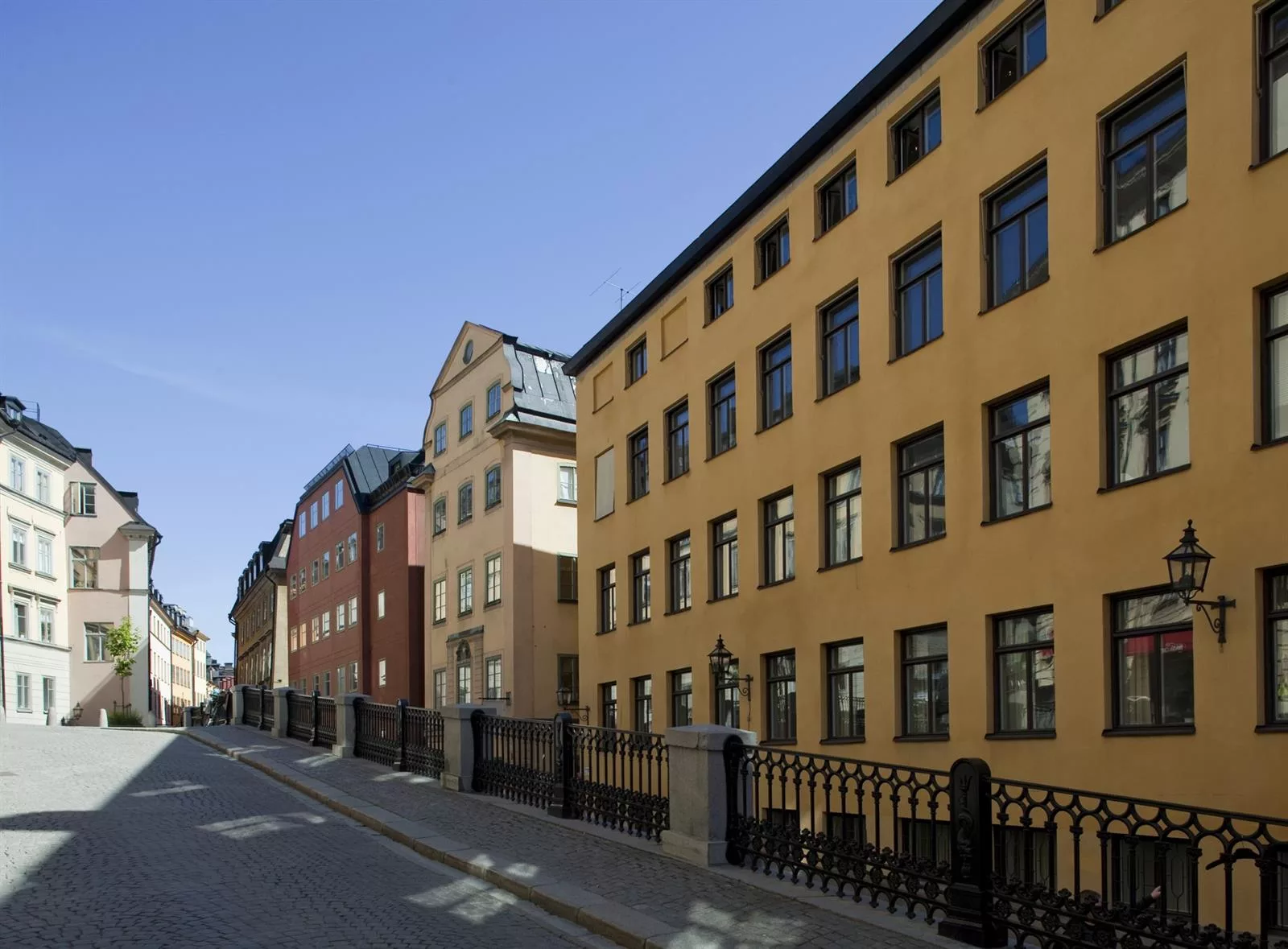 En rad med olika byggnader längs en gata, med en gul byggnad i förgrunden och blå himmel ovanför.
