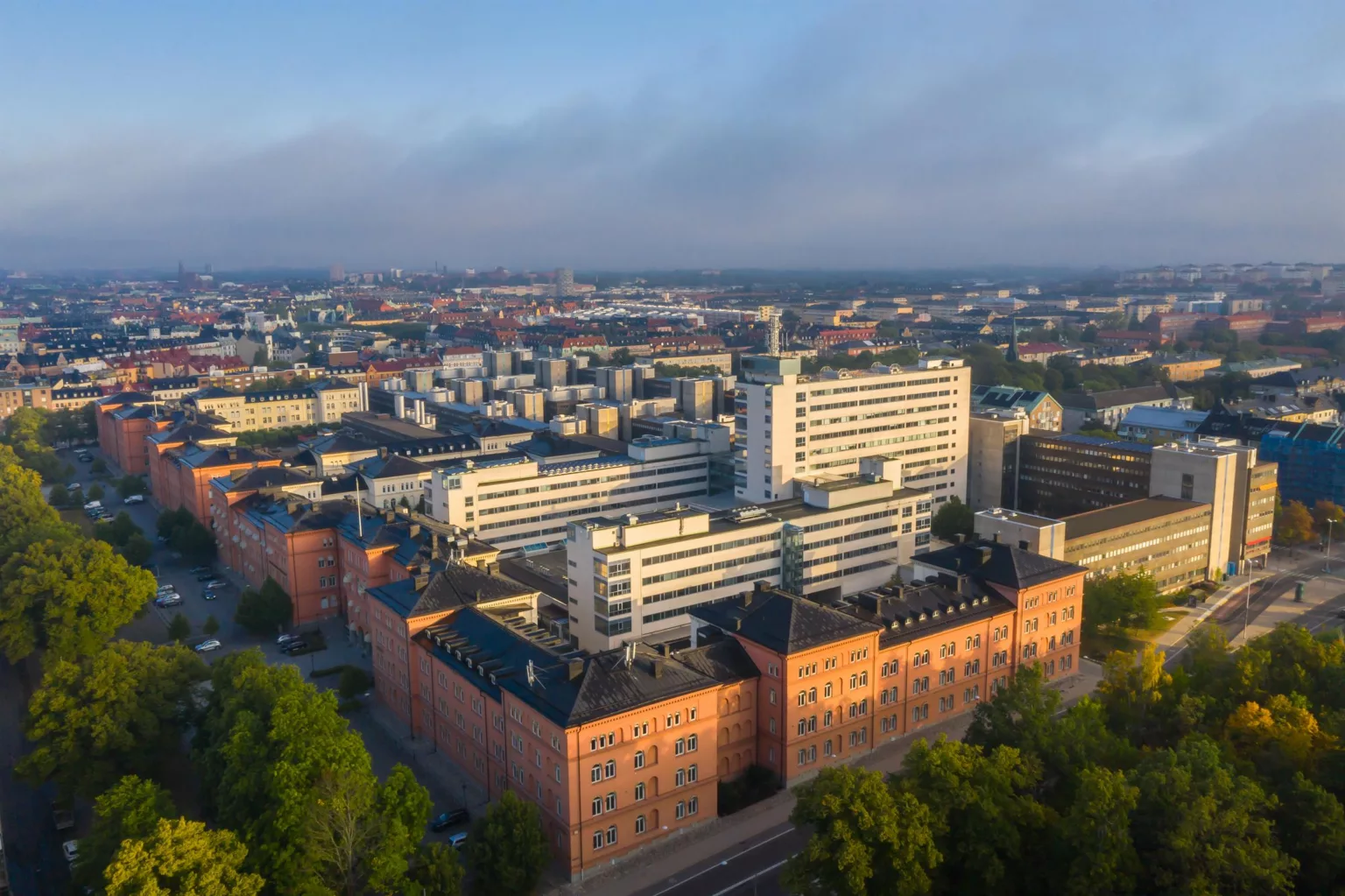 En vy över en stad med flera byggnader, inklusive en stor vit byggnad och äldre tegelbyggnader, under en klar himmel.