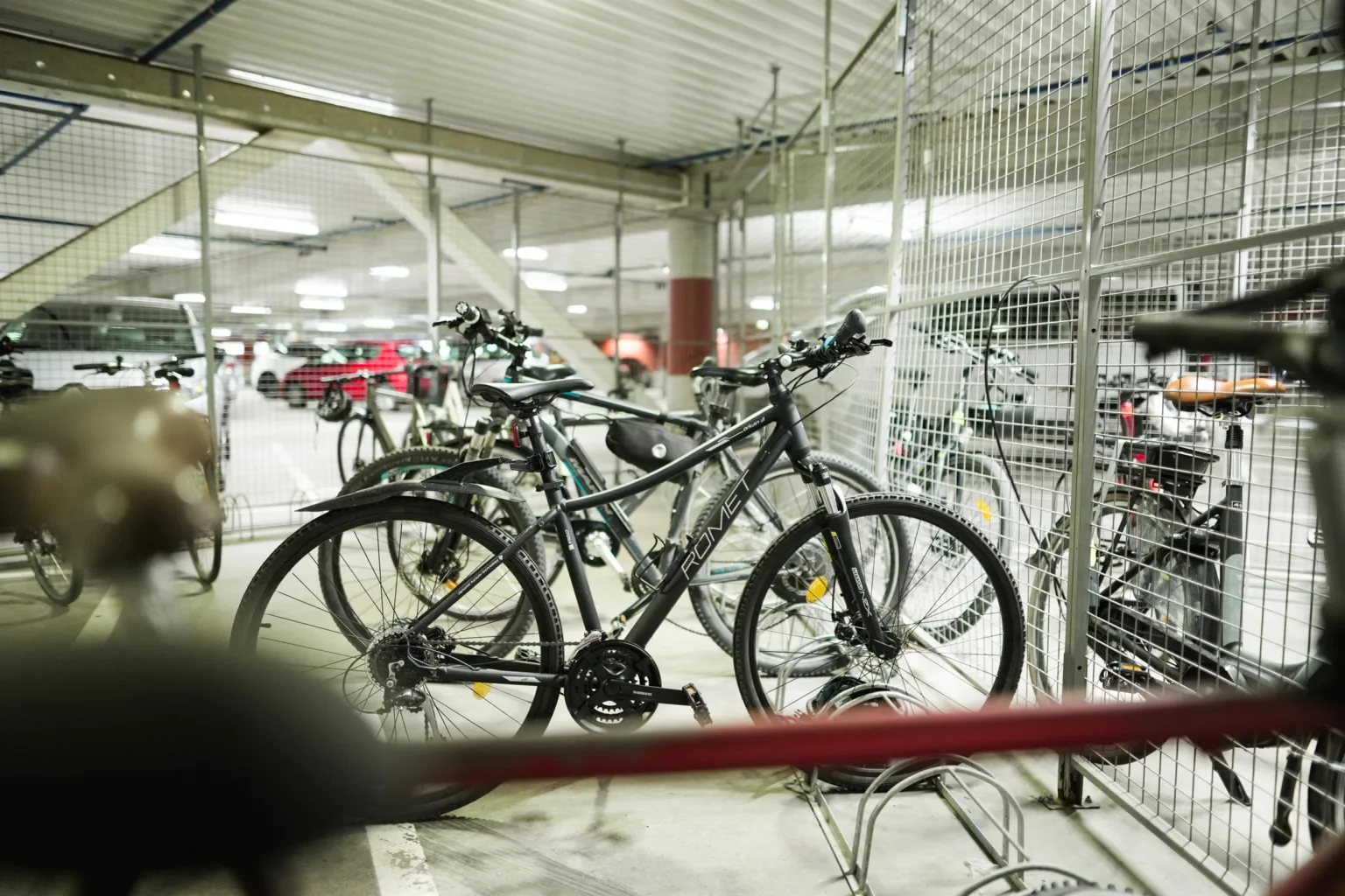 Cykelparkering med flera cyklar uppställda och omgivande metallstängsel i en inomhuslokal.