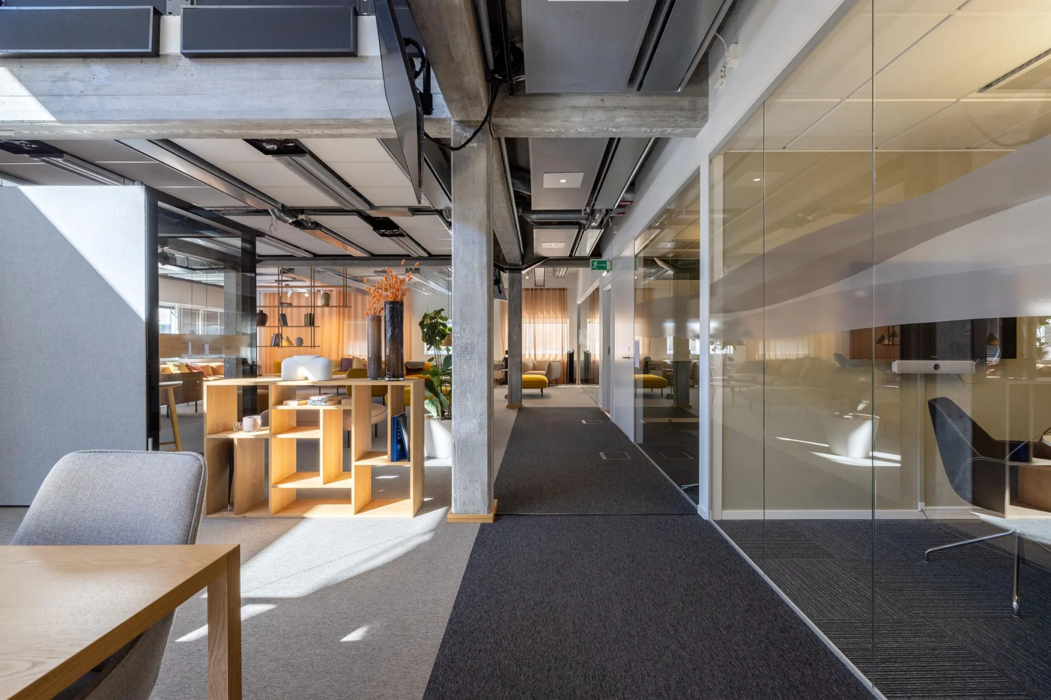 Ett modernt kontorsutrymme med öppna arbetsplatser, glasväggar och industriell design.