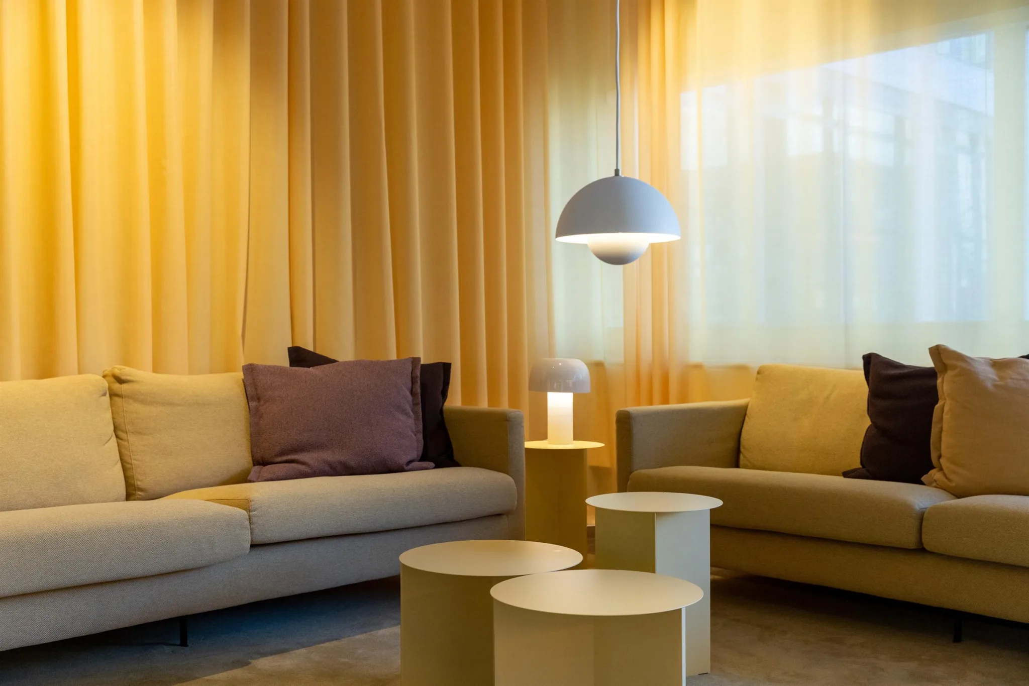 3. En mysig lounge med soffor, ett soffbord och en hängande lampa, omgiven av gula gardiner.