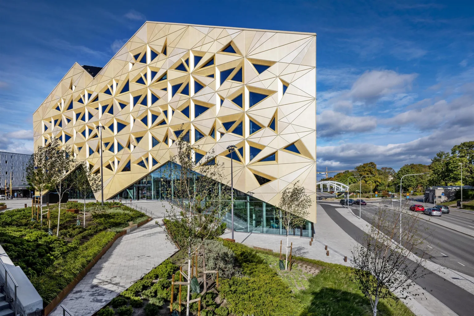 4. En byggnad med unik geometrisk fasad i trä, omgiven av grönska och gångvägar.