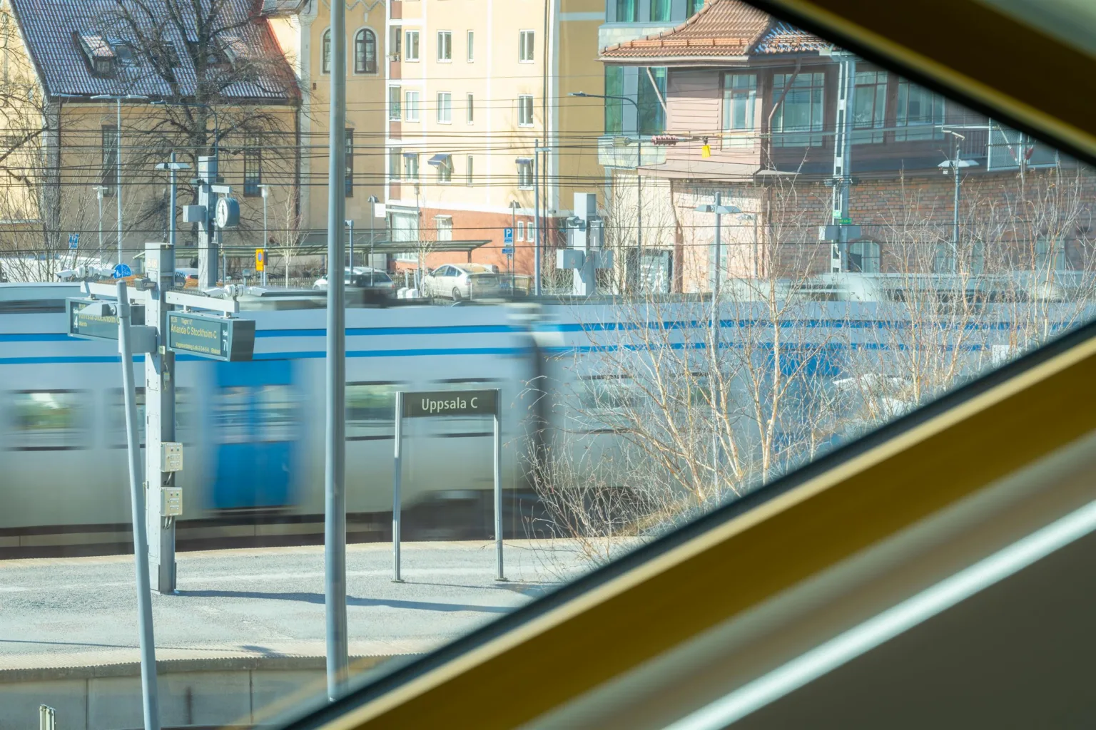 Utsikt genom ett trekantigt fönster som visar en blåvit spårvagn och omgivande byggnader.