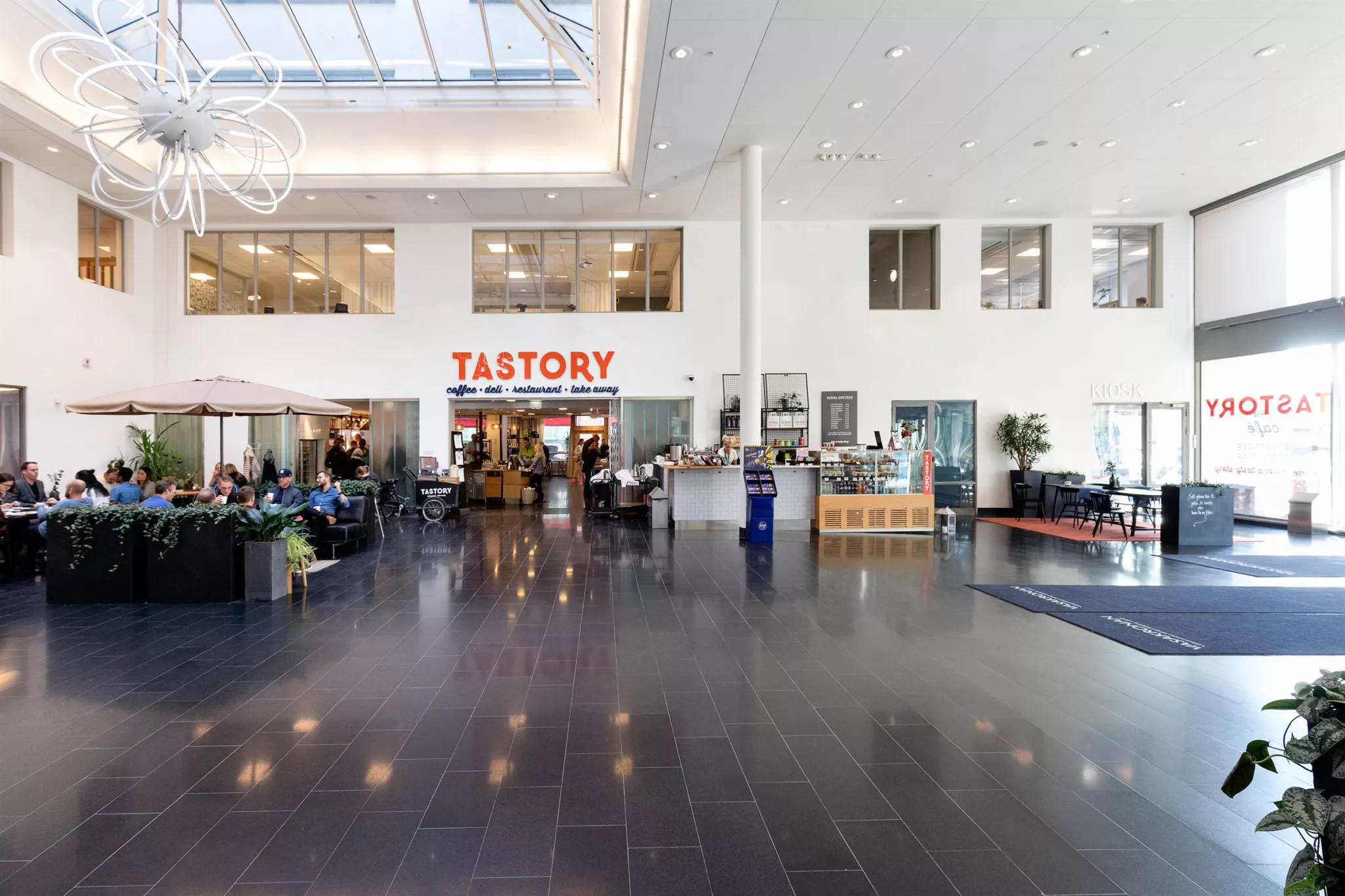 En ljus och rymlig interiör med kaféet "Tastory" och människor i en öppen sittplats.