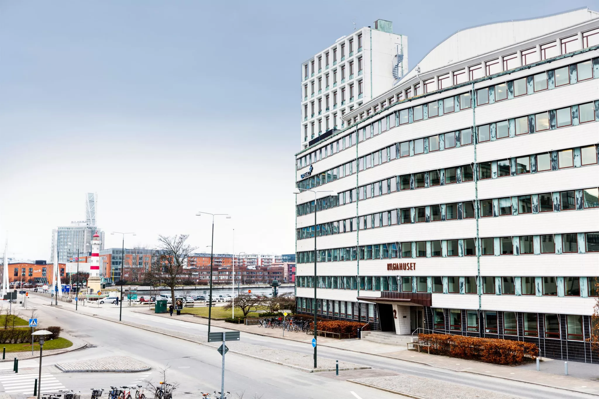 2. En vit byggnad med rundade hörn och glasfönster längs en stadsgata, med träd och gångvägar.