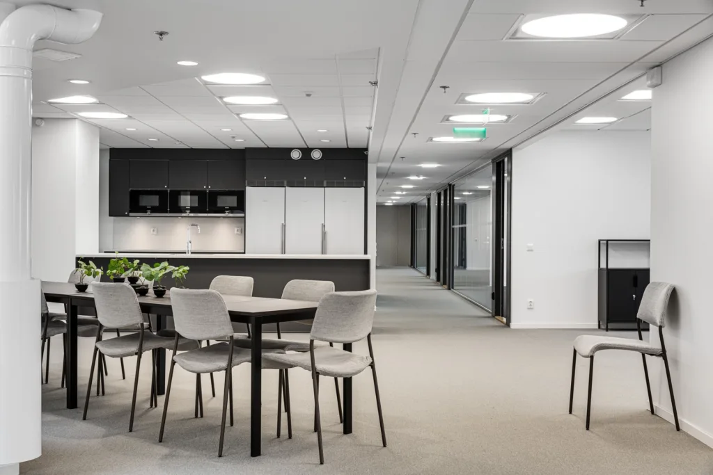 4. Ett modernt pausutrymme med matbord och stolar, ett kök med kylskåp och skåp i bakgrunden.