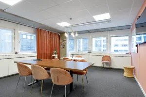 Ett mötesrum med ett långt bord, flera stolar och röda gardiner vid fönstren.
