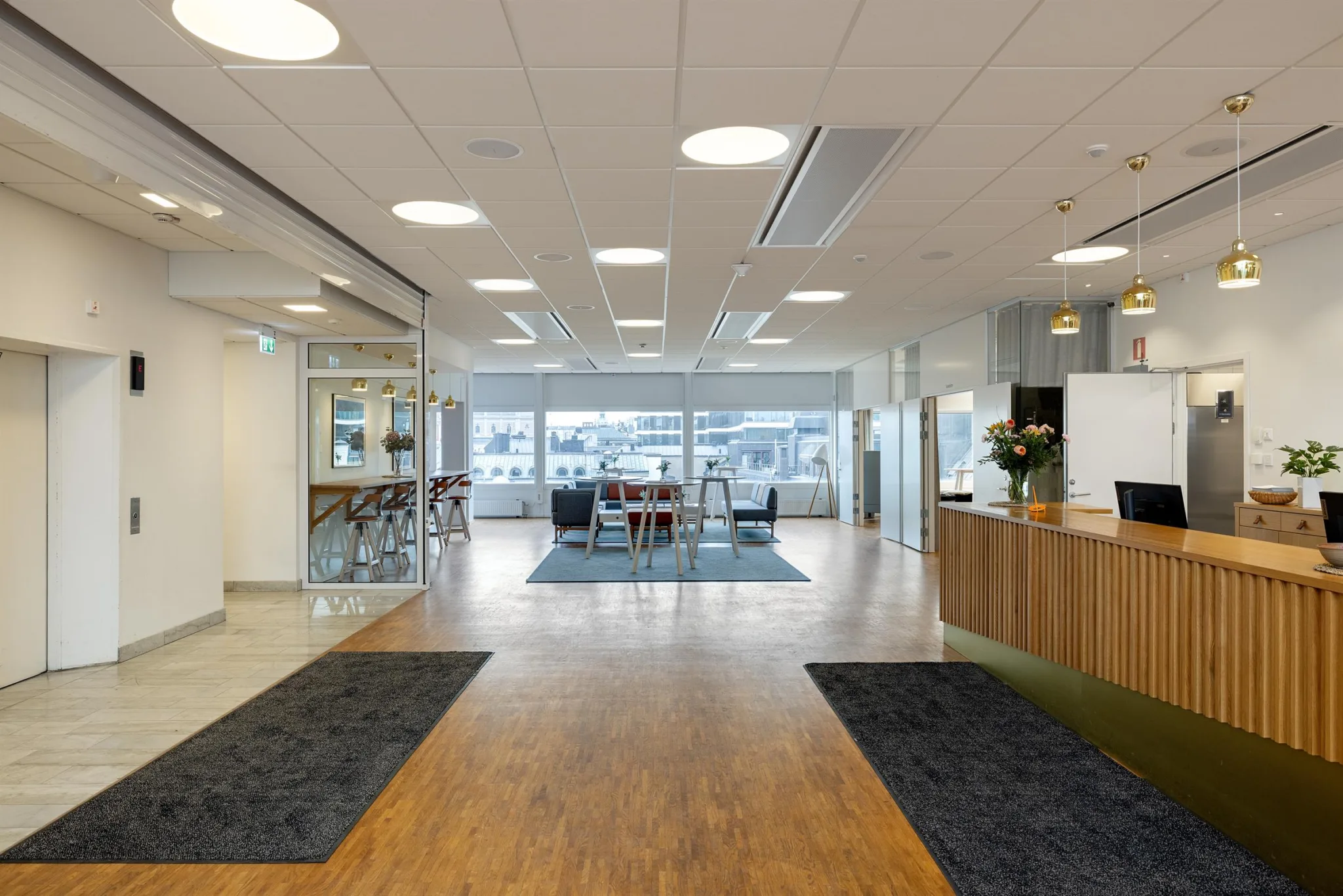 3. Ett ljust kontorsutrymme med trägolv, reception, sittgrupper och stora fönster som släpper in naturligt ljus.