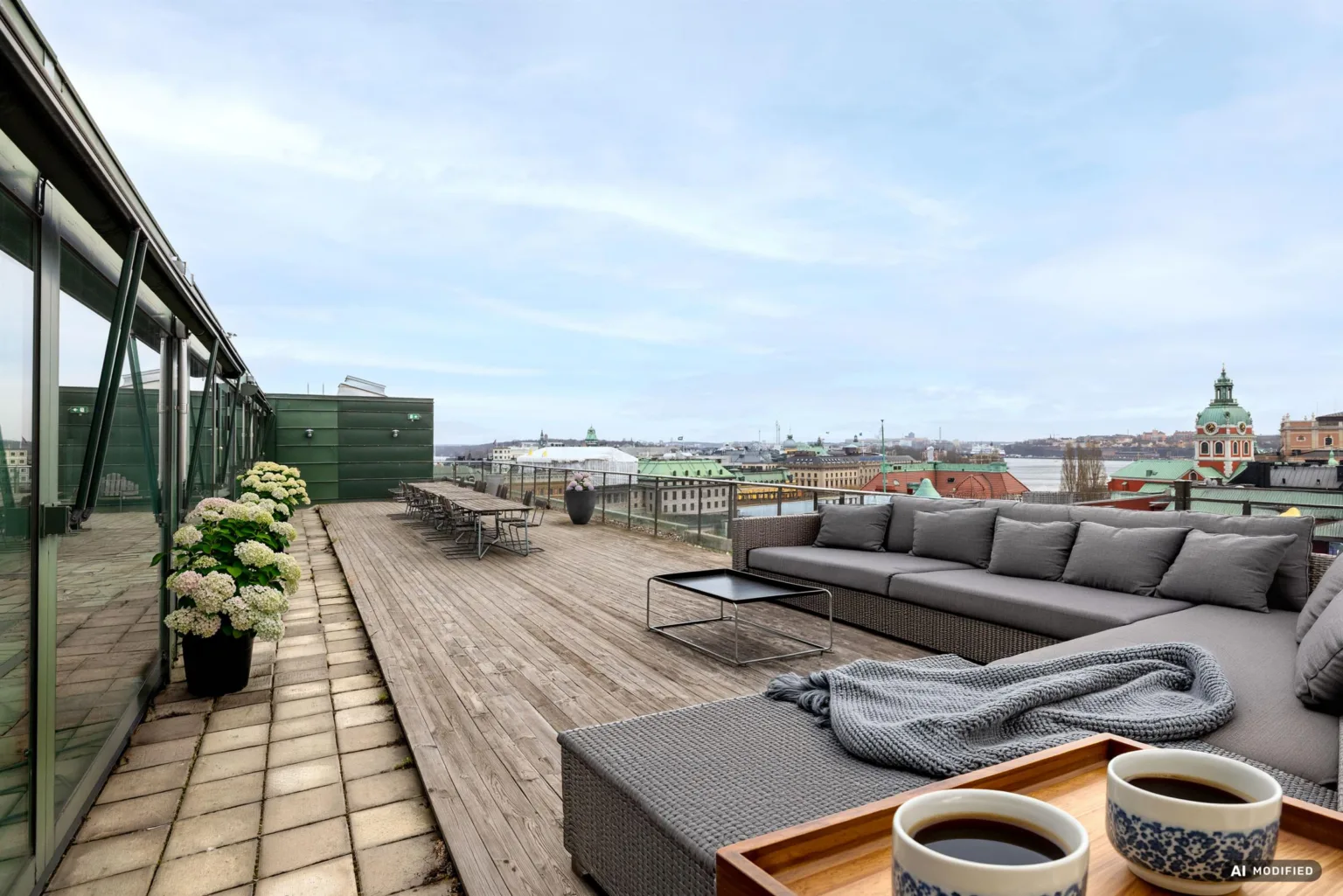 2. En stor takterrass med trätrall, soffor, bord och utsikt över stadens takåsar.