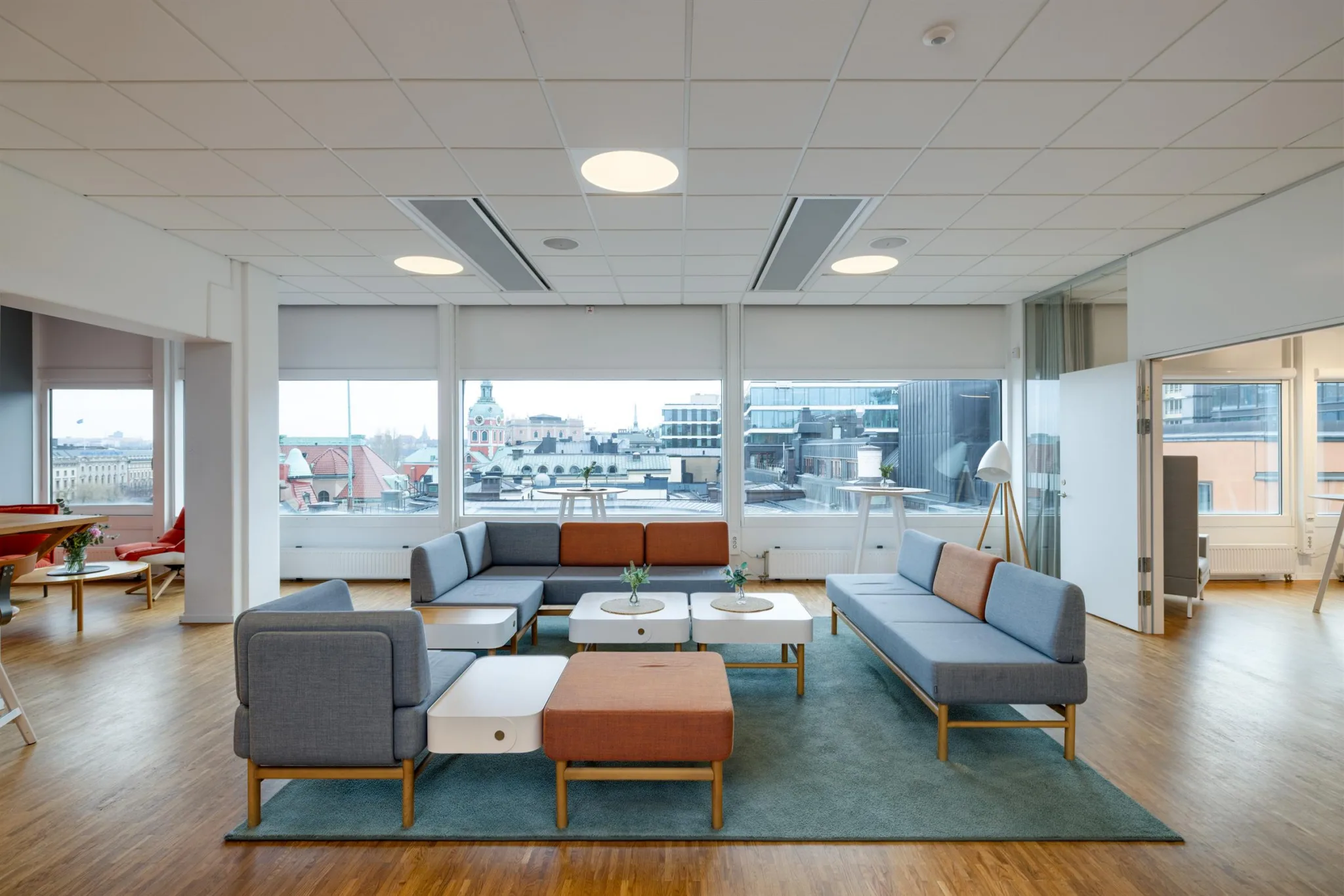1. En modern sittgrupp med soffor och bord i ett ljust rum med stora fönster som visar en stadsvy.