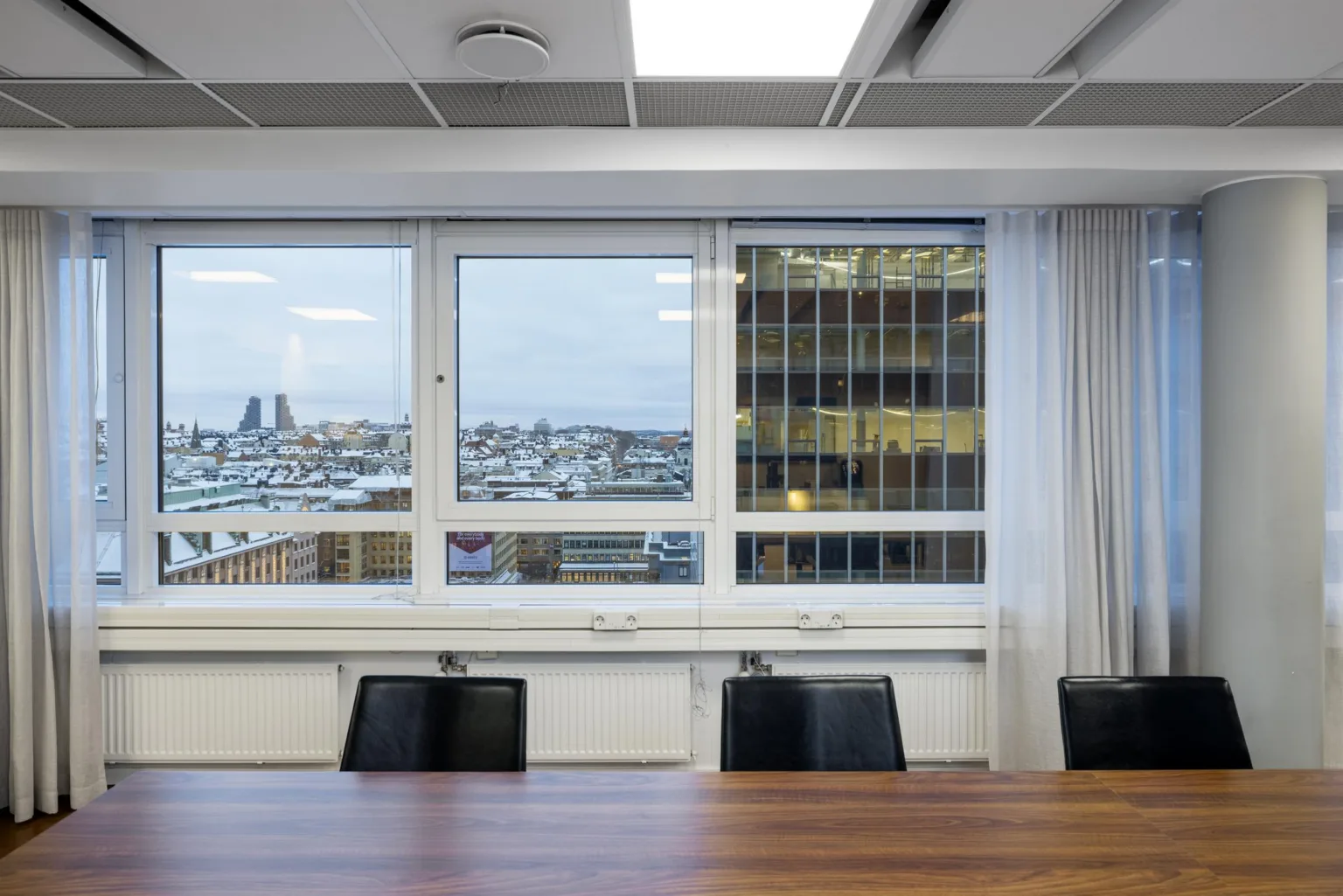 Ett mötesrum med ett stort bord, stolar och fönster som visar stadens skyline.