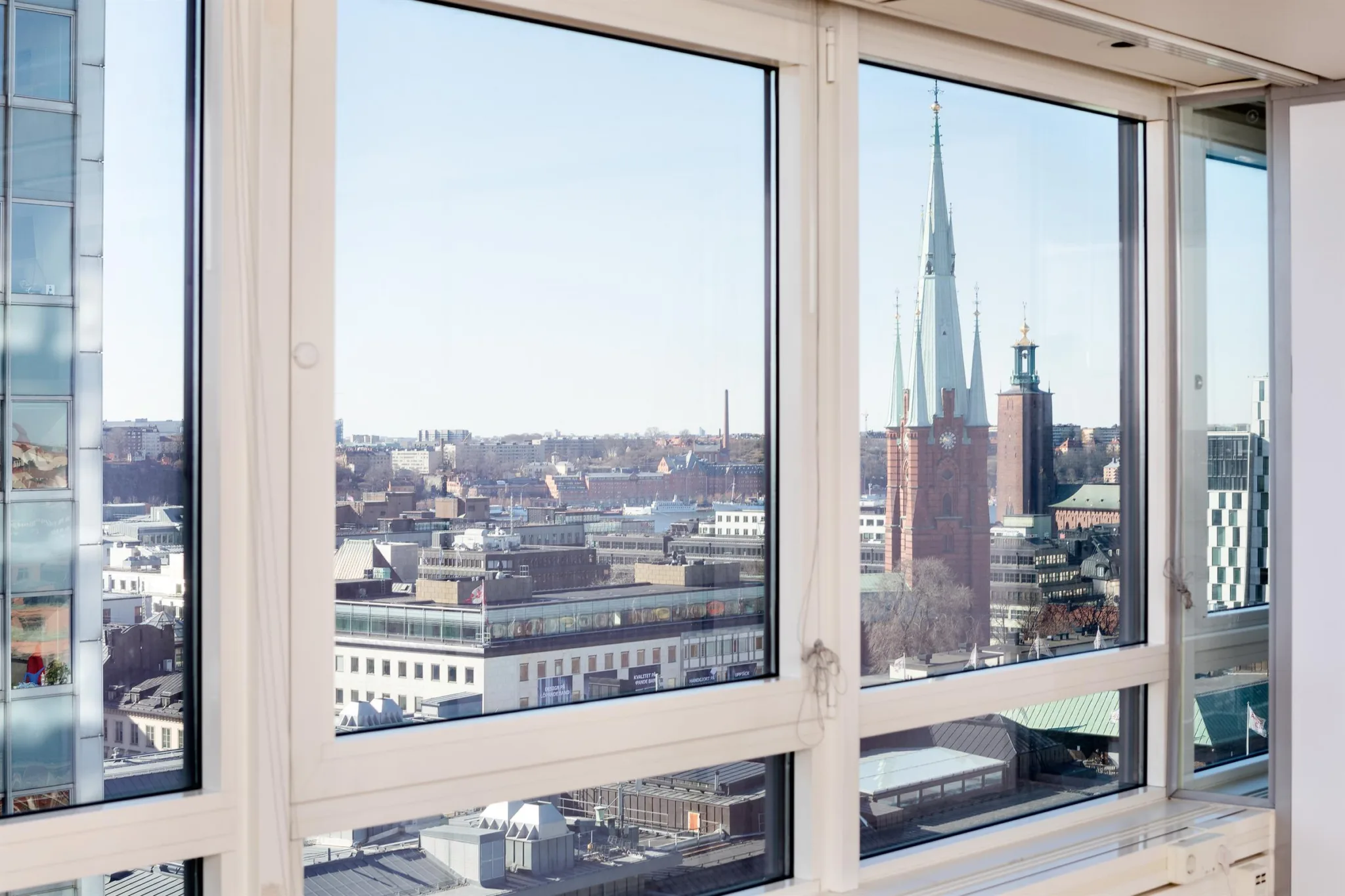 2. Utsikt genom ett fönster med byggnader och kyrktorn som syns på avstånd under en klar himmel.