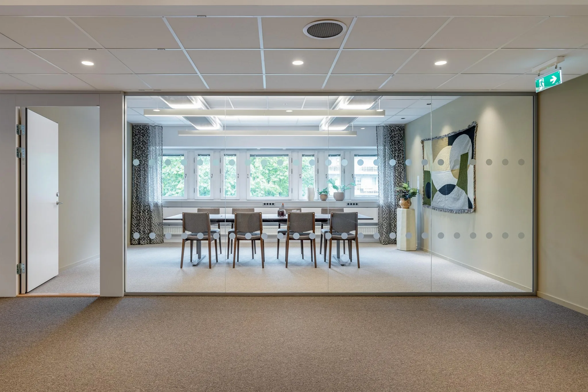 Ett modernt konferensrum med ett glasparti, ett långt bord, stolar och konst på väggen.