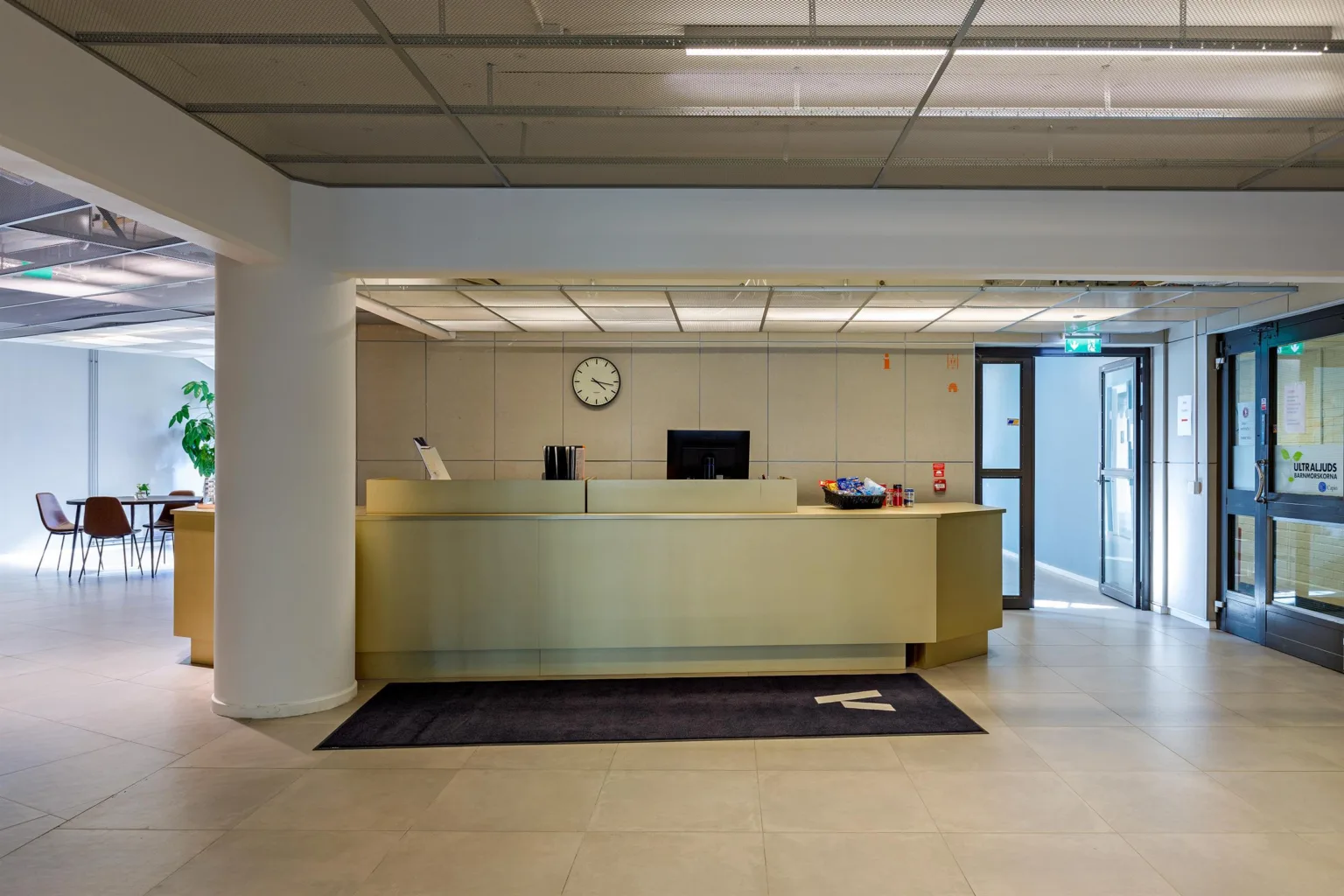 En reception med en ljus disk, en klocka på väggen och glasdörrar i bakgrunden.