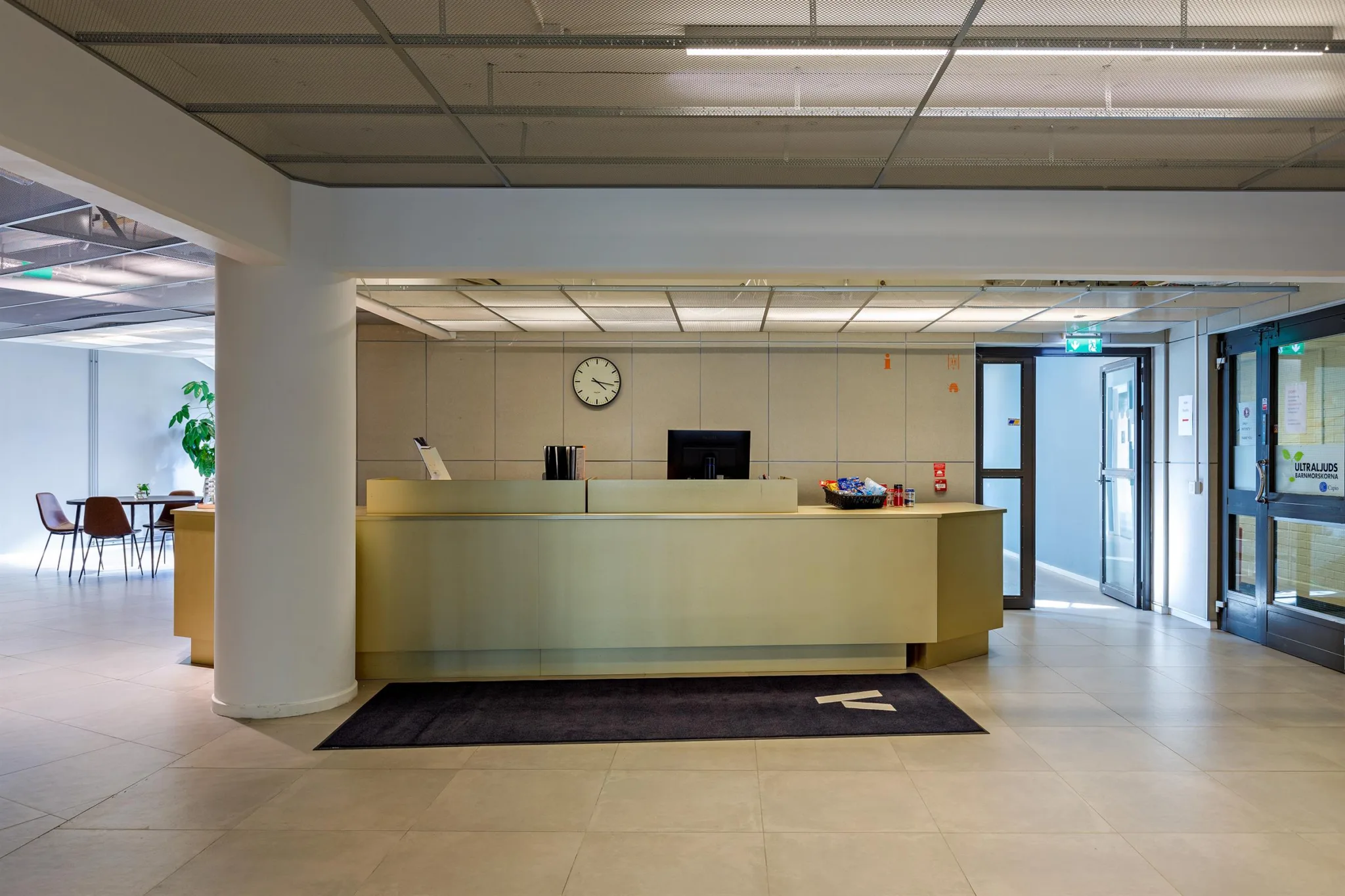 En reception med en ljus disk, en klocka på väggen och glasdörrar i bakgrunden.