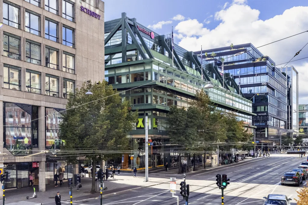 5. En grön byggnad med glasfasad och skyltar, belägen vid en korsning med gående och stadstrafik.