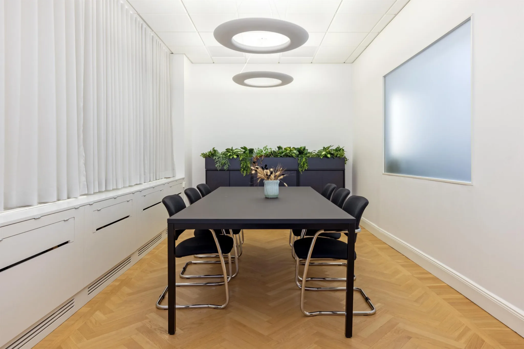 4. Ett konferensrum med svart bord, svarta stolar och växter längs väggen.