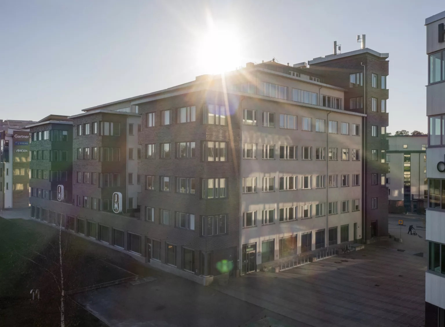 En byggnad med solstrålar som lyser över taket, omgiven av en öppen yta.