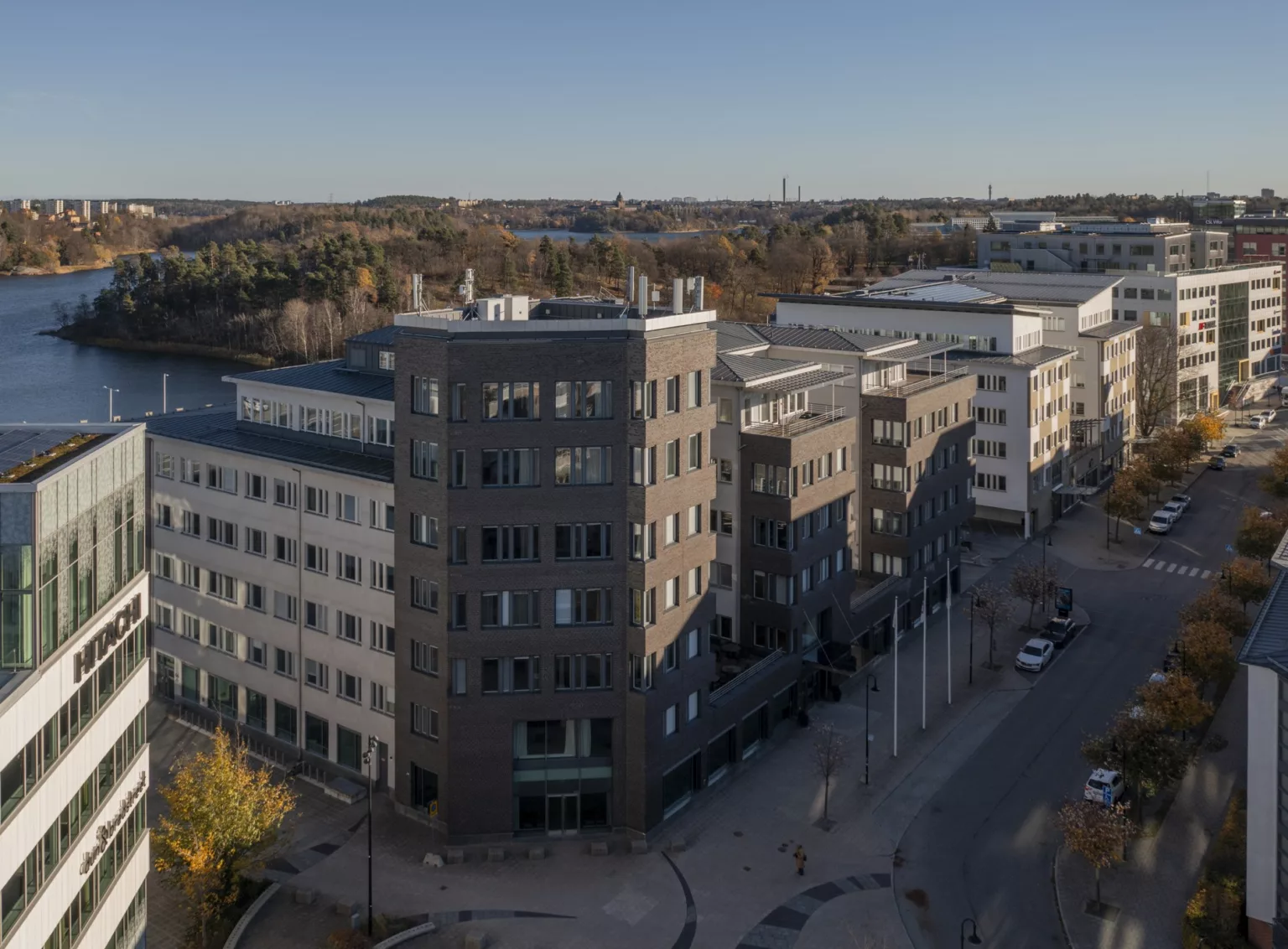 En byggnad med mörk fasad och flera våningar, omgiven av en väg och höstlandskap.
