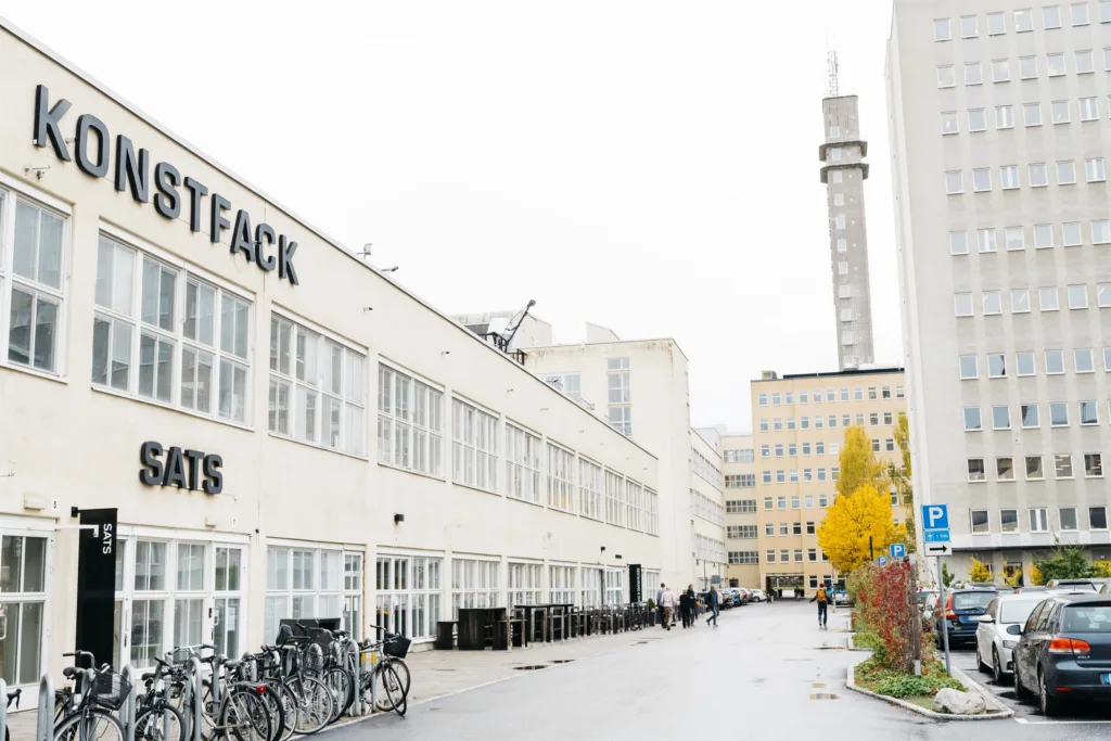 Vit byggnad med texten "STOCKHOLMS UNIVERSITET" på fasaden, cykelställ och en hög mast i bakgrunden.