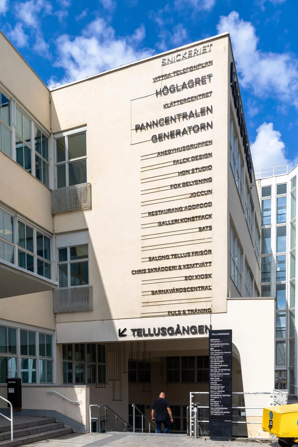 En byggnad med text på fasaden som listar olika avdelningar, inklusive "Högskolan" och "Röntgenavdelningen", och en skylt med "K. Tullusgången" vid entrén.