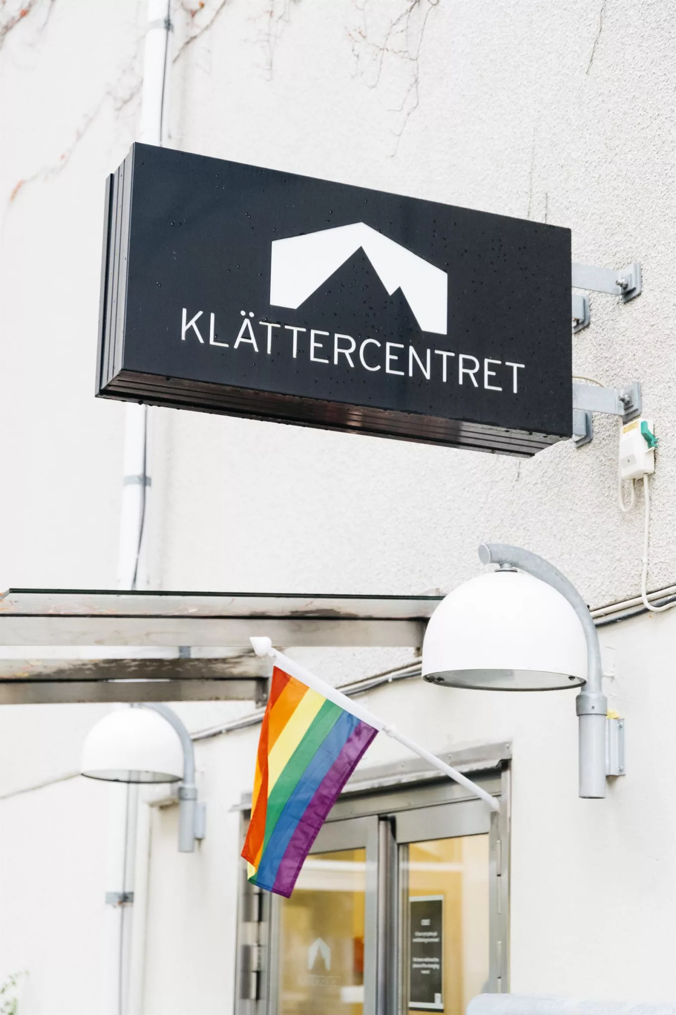 5. En skylt med texten "KLÄTTERCENTRET" och en regnbågsflagga hängande nedanför, på en vit vägg.