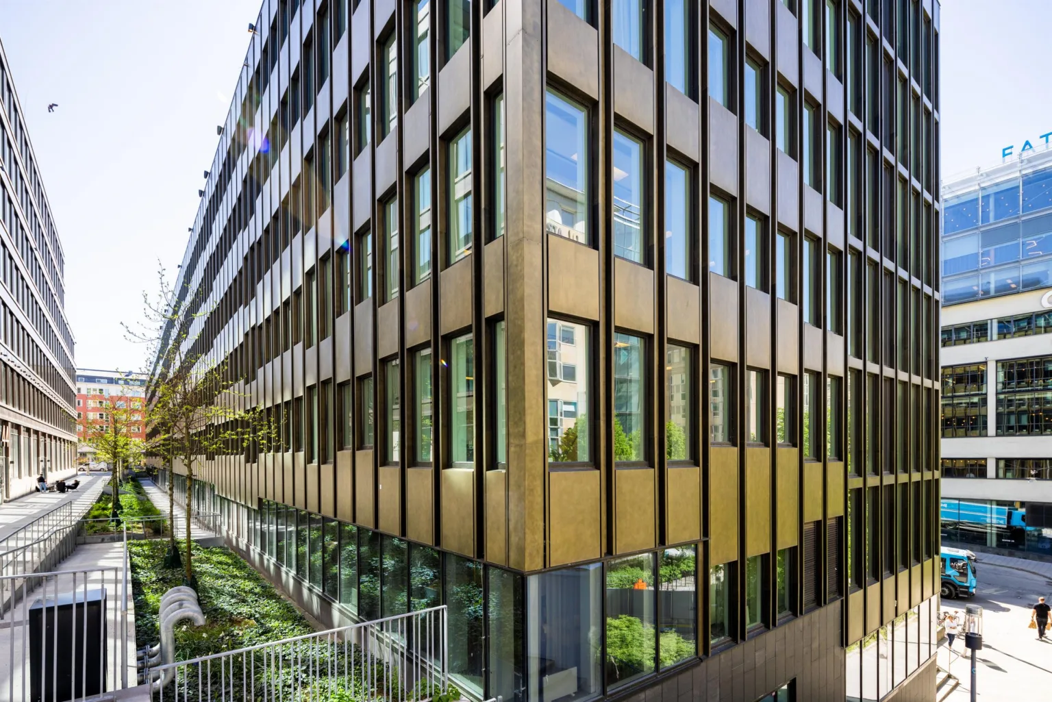 En modern byggnad med fasad av glas och metall, omgiven av grönska och gångbanor.
