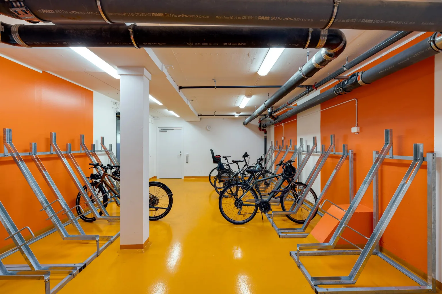 En cykelparkering med orange golv, cyklar och upphängningsställ för cyklar.