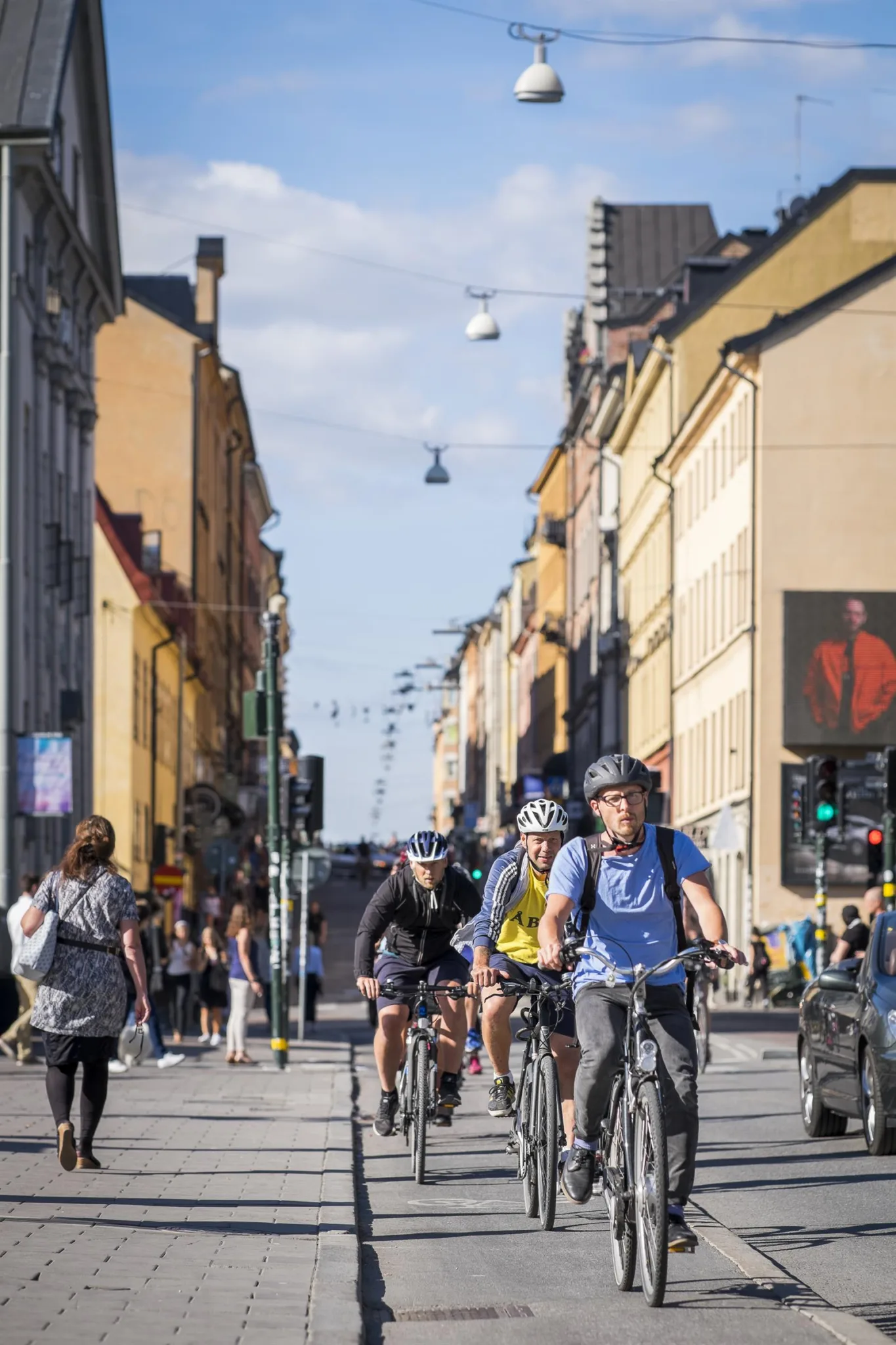Cyklande personer på en stadsgata omgivna av byggnader och fotgängare.