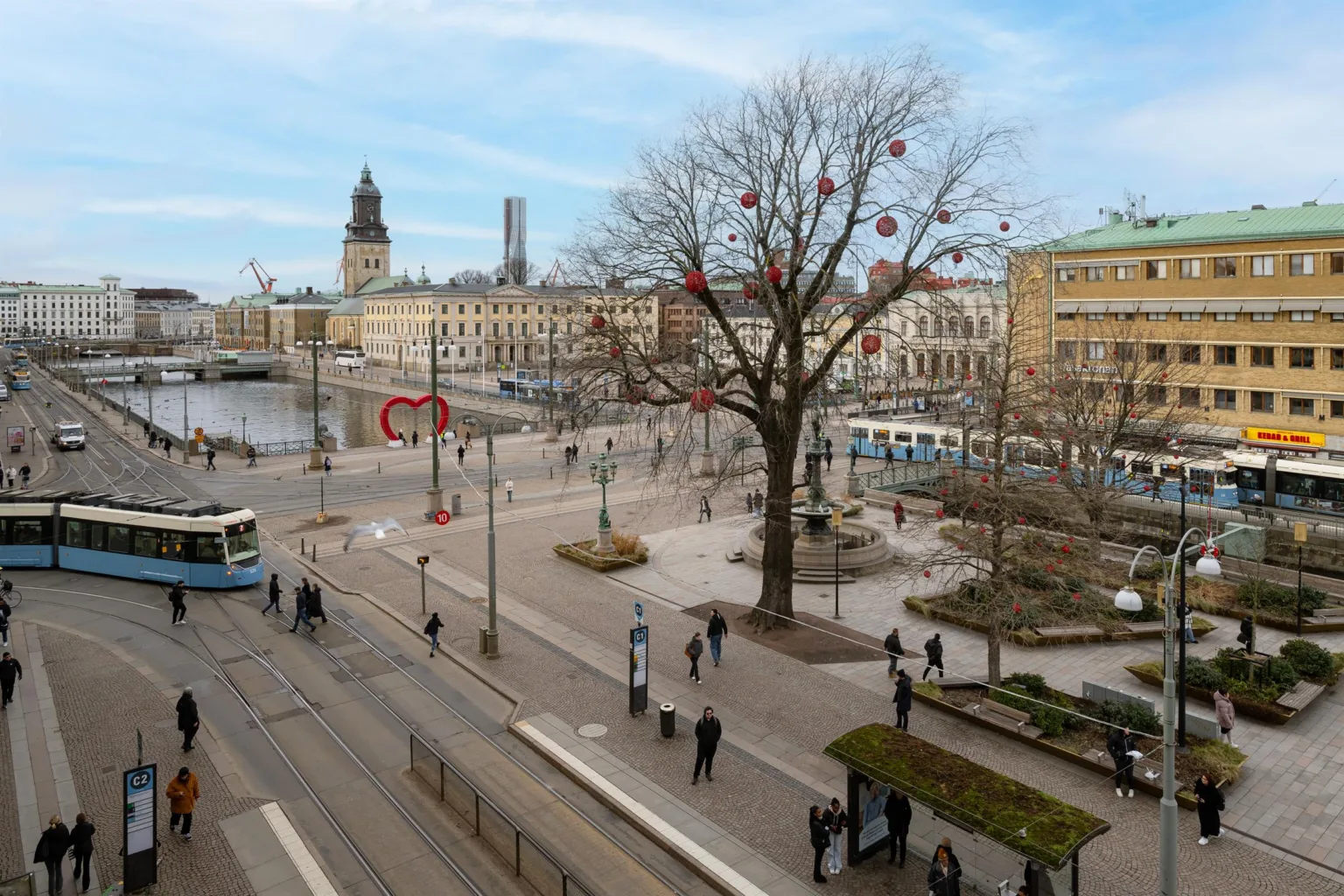 2. Ett torg med träd dekorerade med röda prydnader, spårvagnar och omgivande byggnader.
