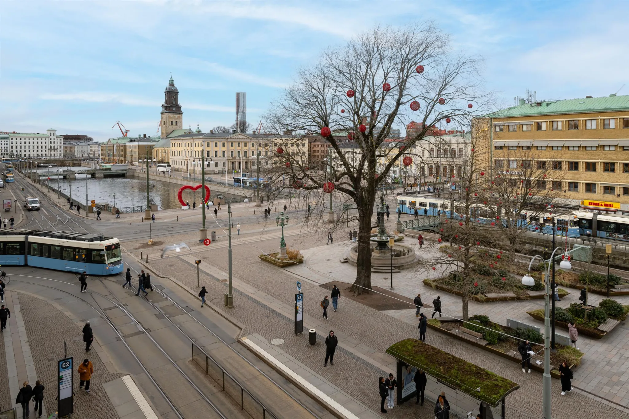 2. Ett torg med träd dekorerade med röda prydnader, spårvagnar och omgivande byggnader.