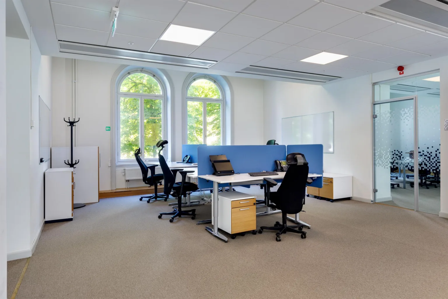 Ett modernt kontor med flera arbetsstationer, svarta stolar och stora fönster som släpper in dagsljus.