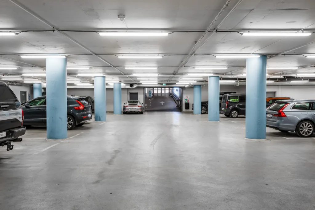 En underjordisk parkeringsplats med blåa pelare, parkerade bilar och stark belysning.
