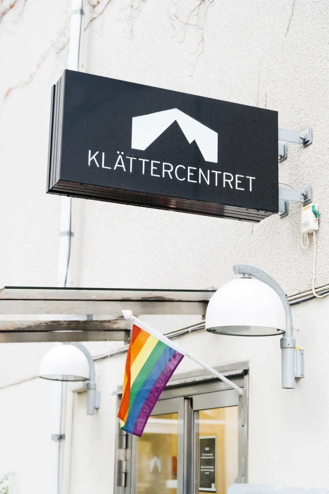1. En skylt med texten "Klättercentret" och en takformad symbol, med en regnbågsflagga hängande nedanför.