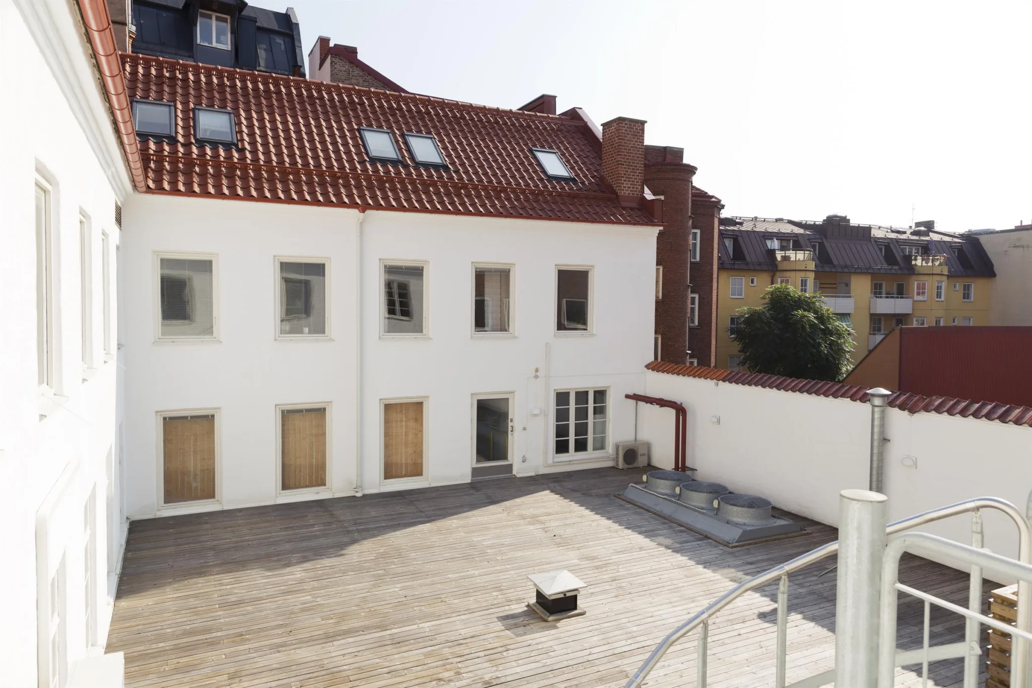 En rymlig innergård med en vit byggnad i bakgrunden, röda takpannor och flera fönster.