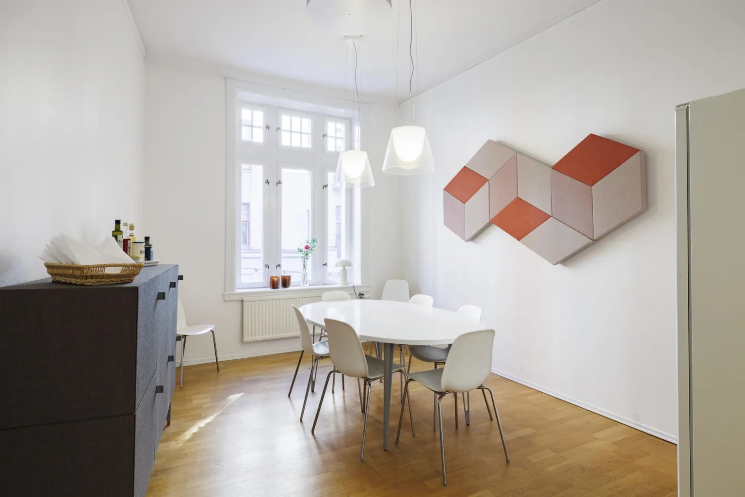 4. Ett matrum med vitt bord, vita stolar och geometrisk väggkonst i rött och beige.