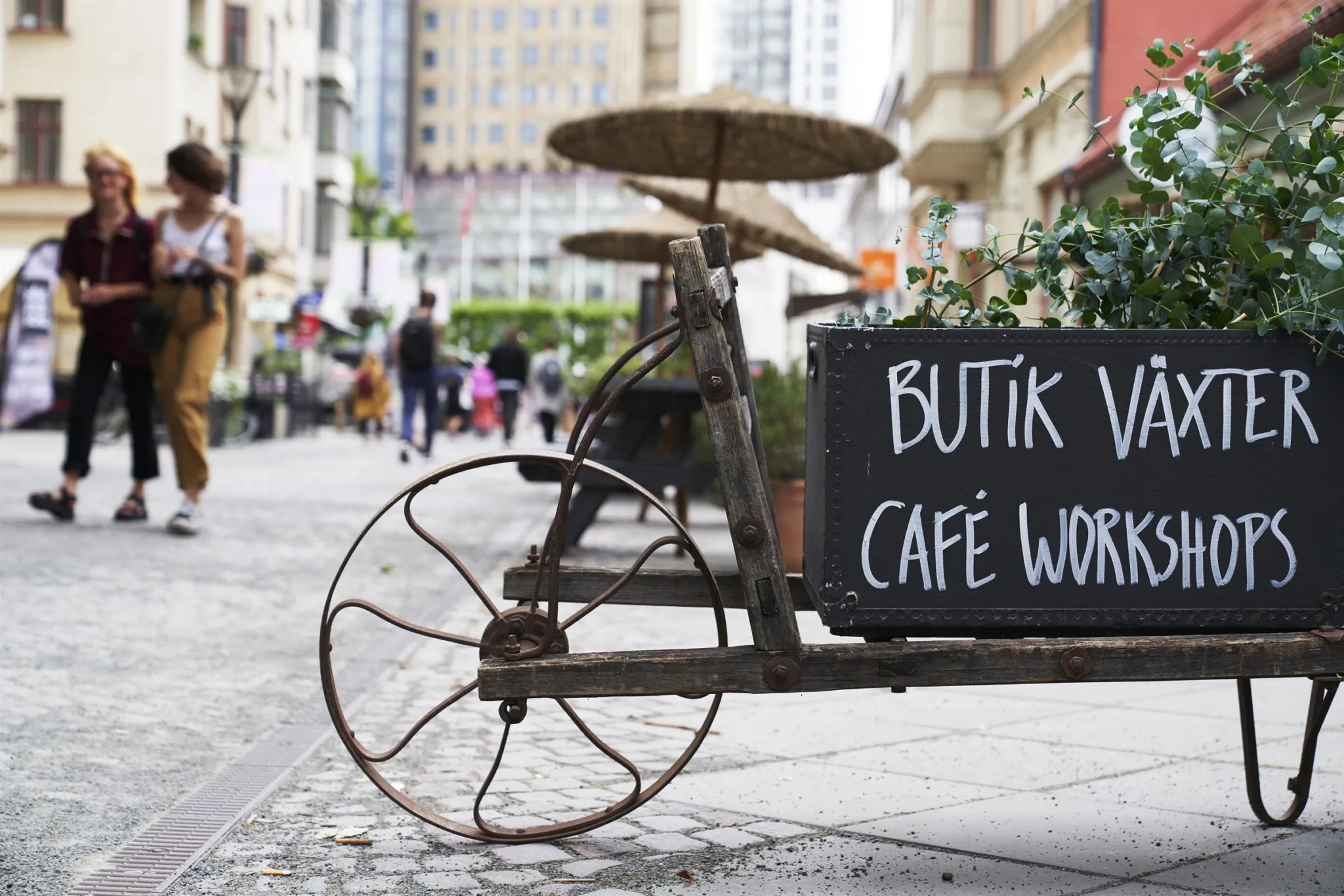 2. En gammaldags cykel med en svart skylt som visar texten "Butik & Café Workshop" står på en stenlagd gata med människor i bakgrunden.