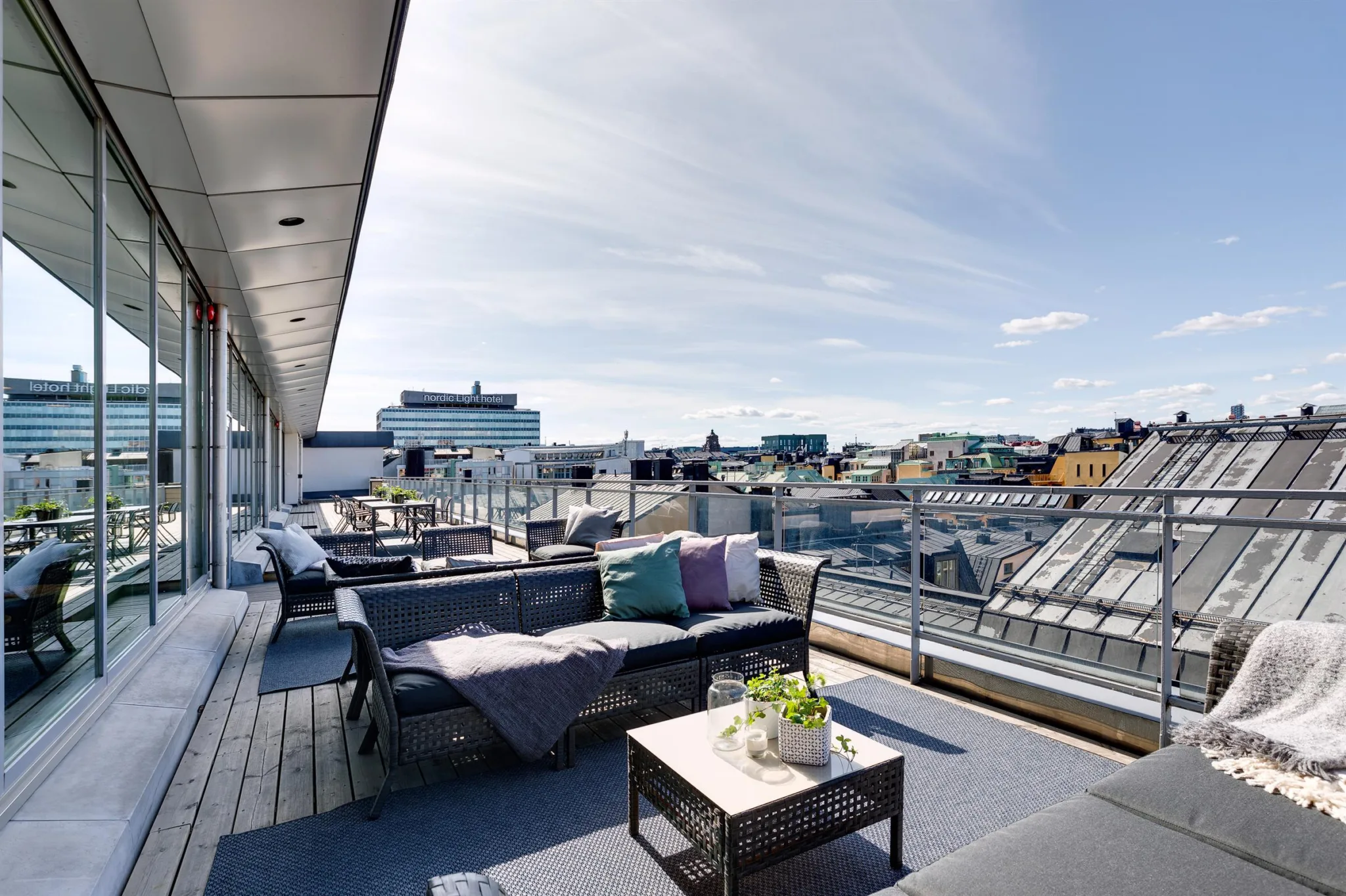 En takterrass med sittgrupper, utsikt över stadens byggnader och klarblå himmel.