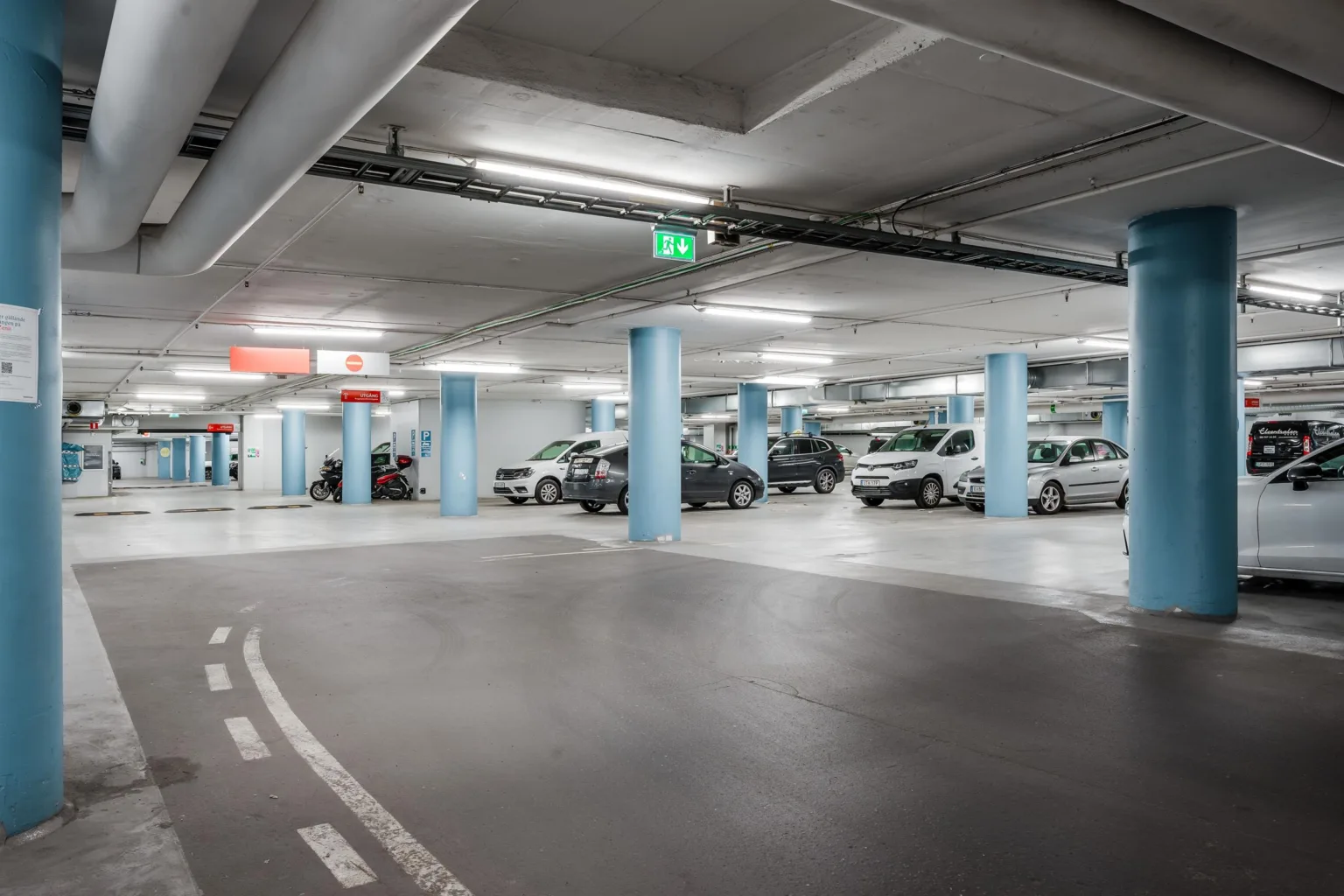 En parkeringsgarage med flera parkeringsplatser fyllda med bilar och blå pelare.