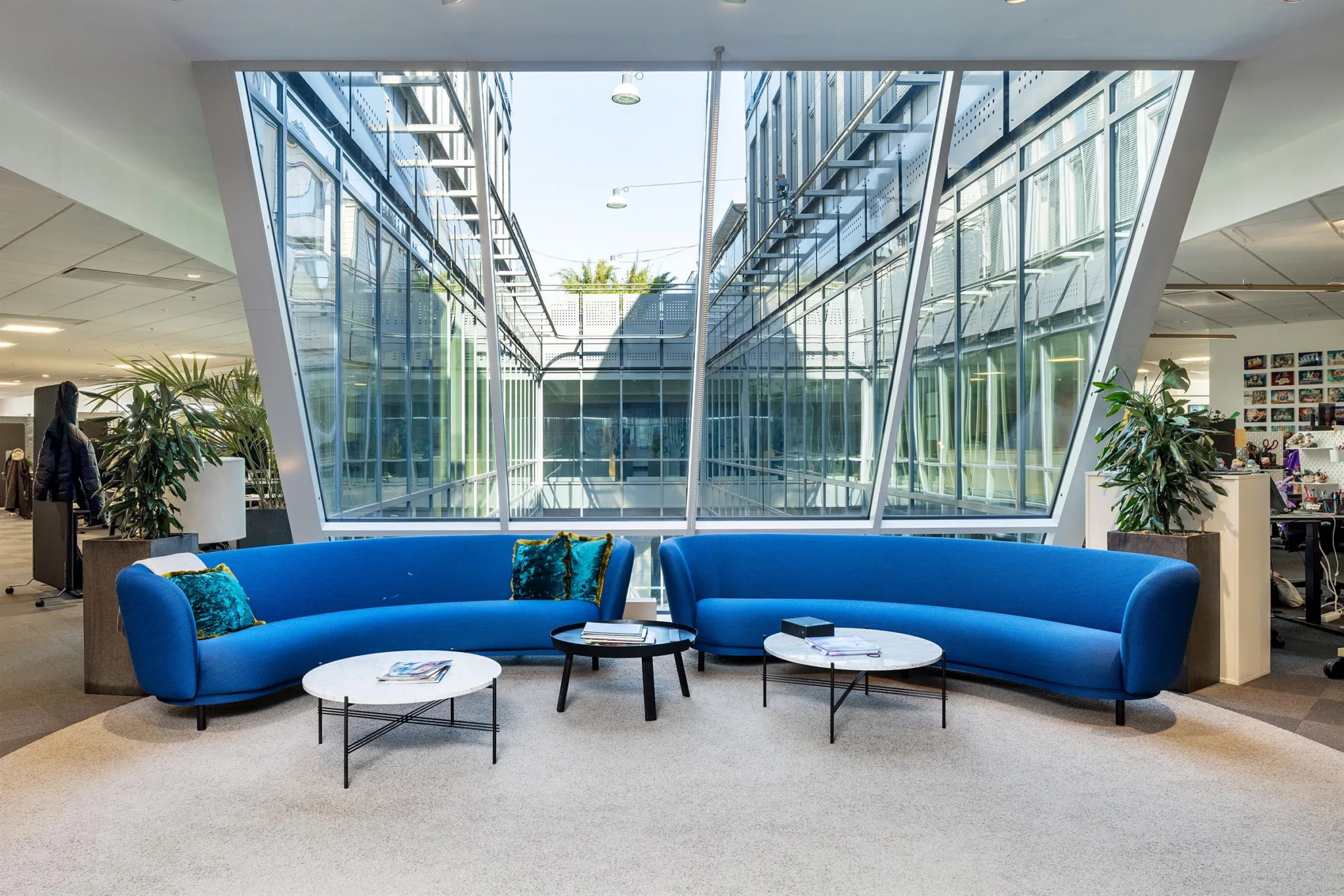 Modern lounge med blå soffor, små runda bord och glasväggar som släpper in dagsljus.